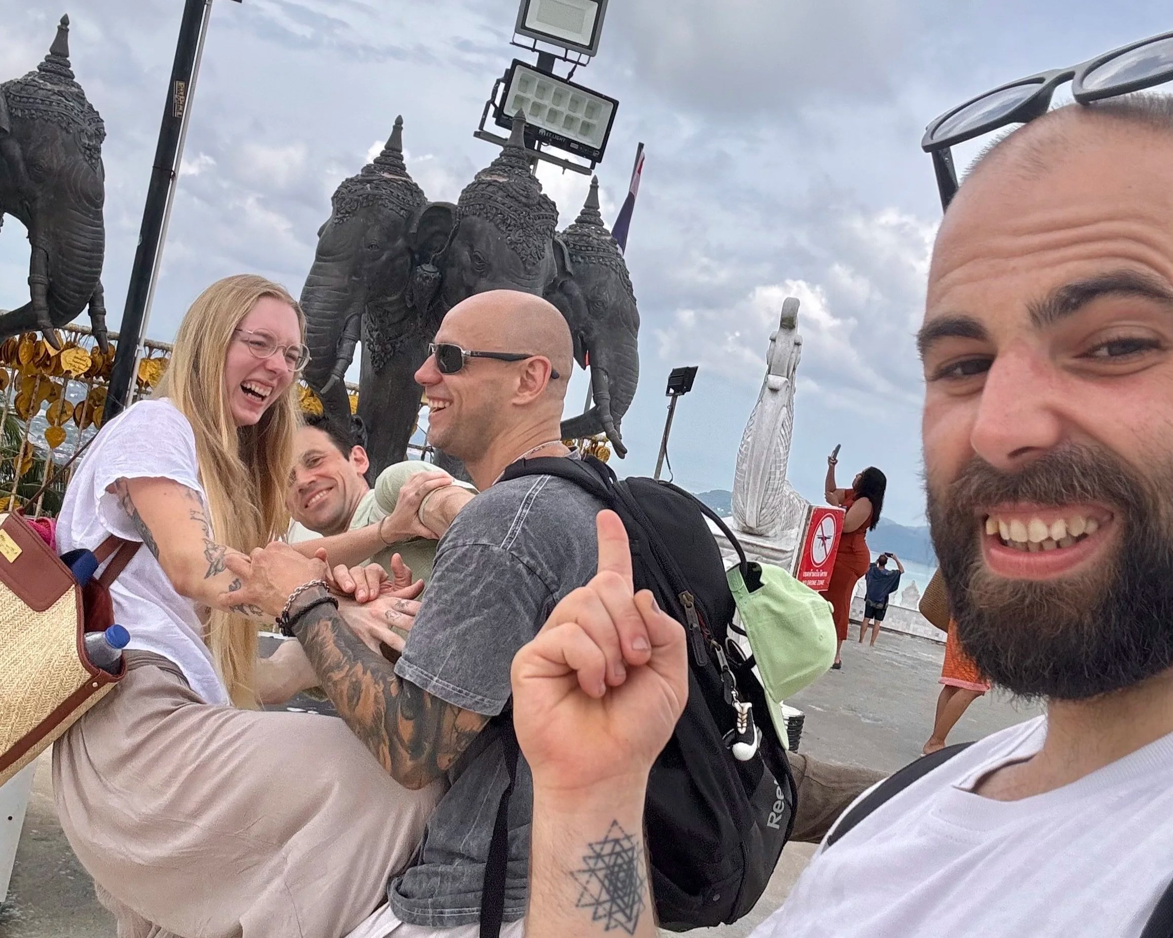 Four people smiling and laughing at a seaside location with statues of elephants and a woman in a yoga pose in the background