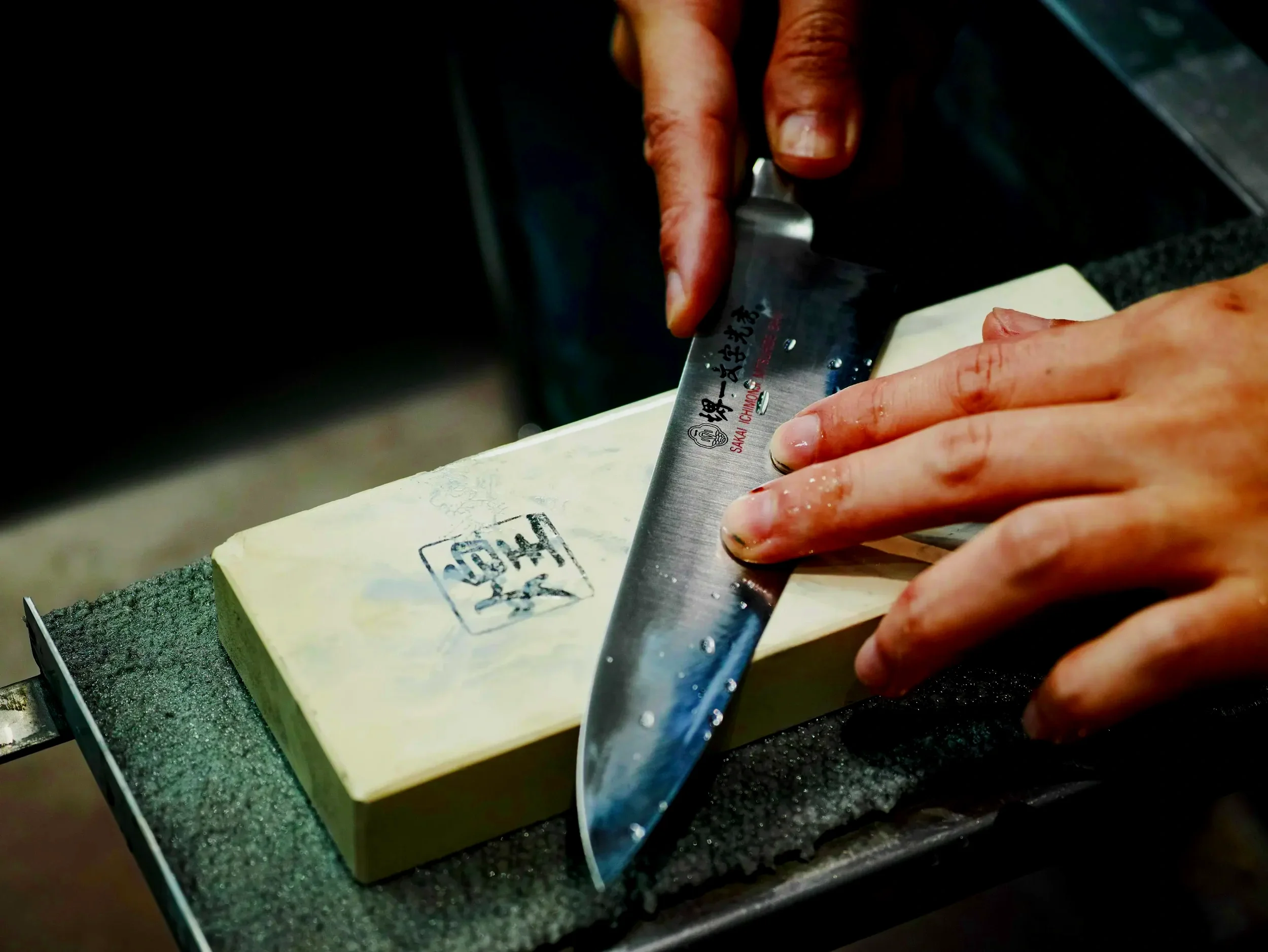 Hands slicing a block of cheese with a Chinese chef's knife.