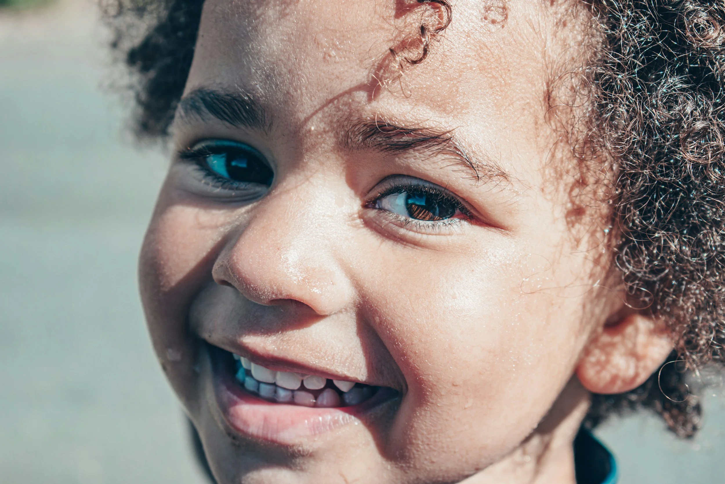 Close-up of a young girl with curly hair smiling outdoors.