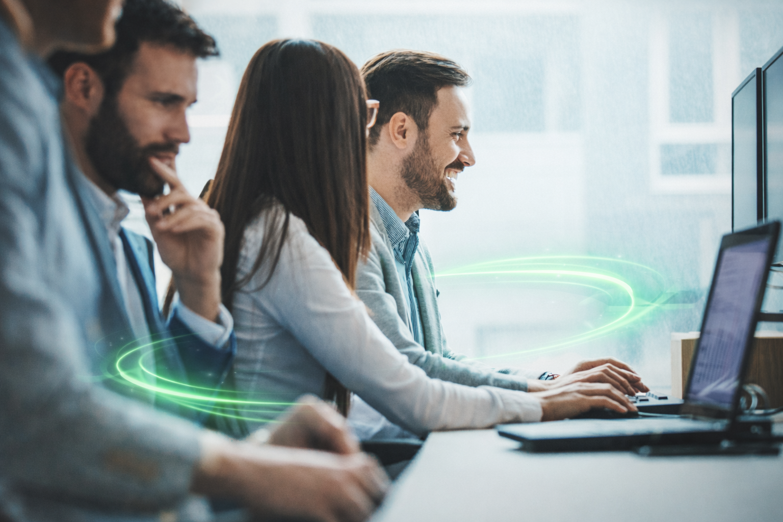 Four people working on computers in an office, with green digital swirl effects added.