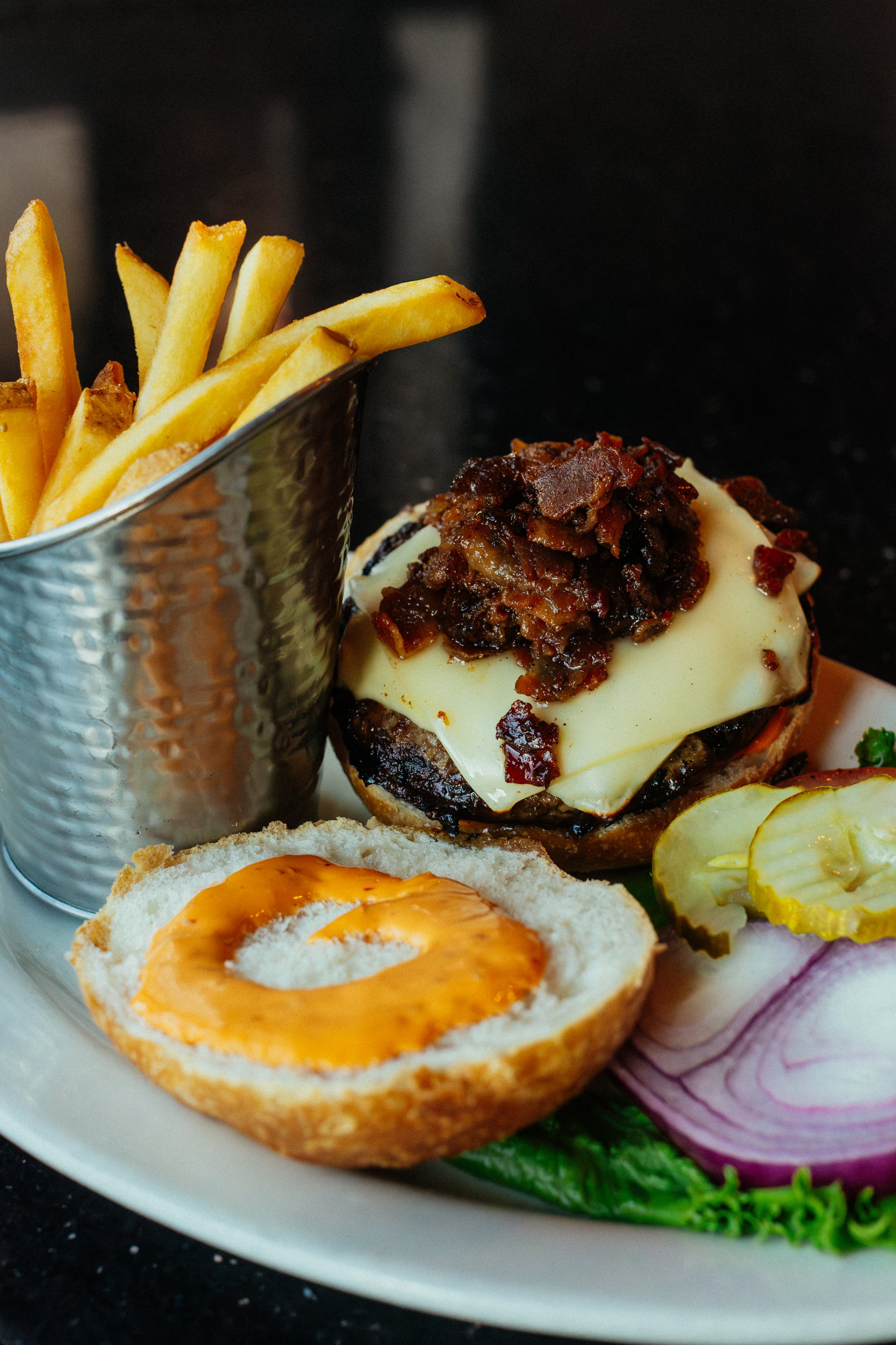 Plate with French fries, cheeseburger with onion and cheese, pickle slices, and sliced red onions.