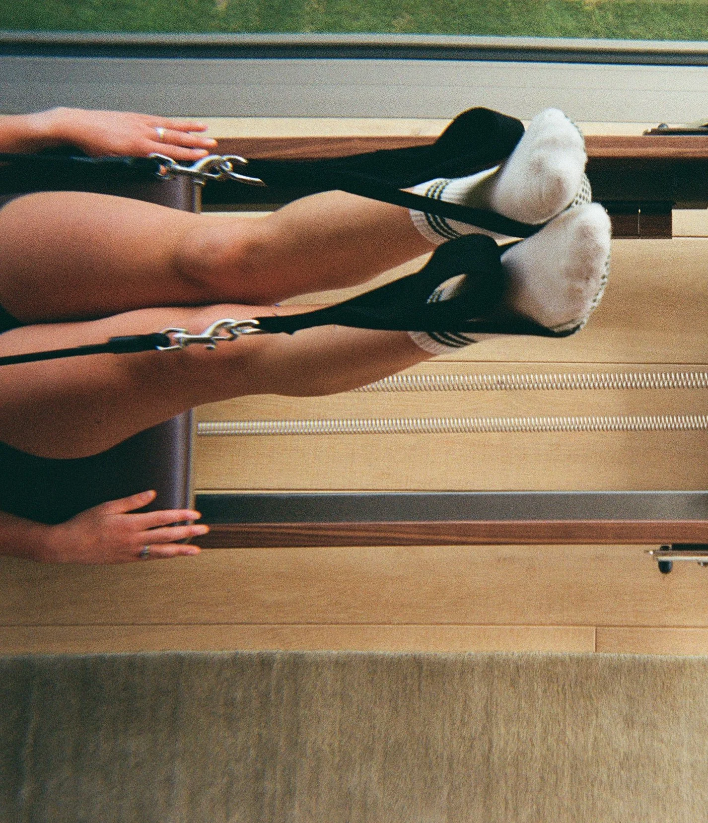 A person lying on their back on a hospital bed with feet elevated, wearing white socks with black stripes at the top, using a traction mechanism with black straps attached to their legs.