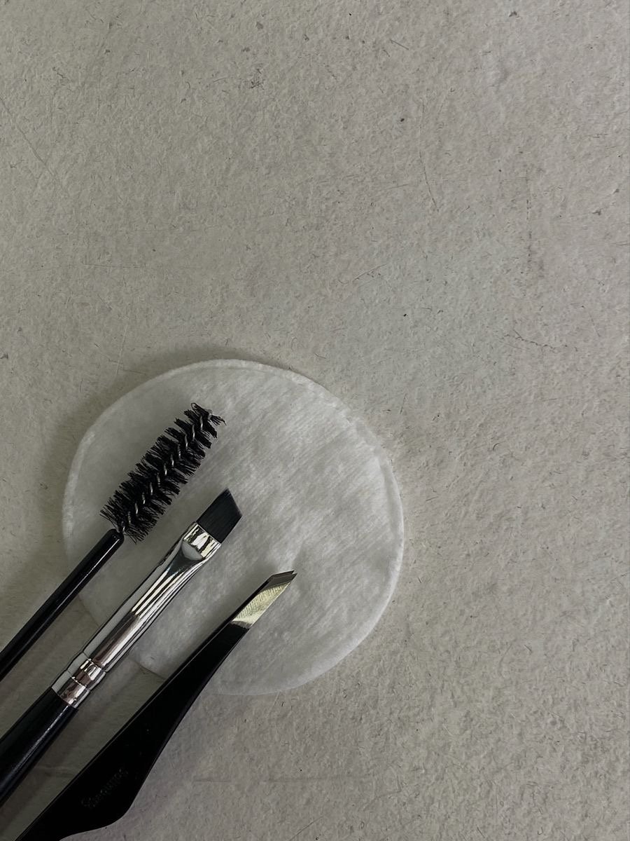 Makeup brushes and tools on a round white cotton pad on a light-colored surface.