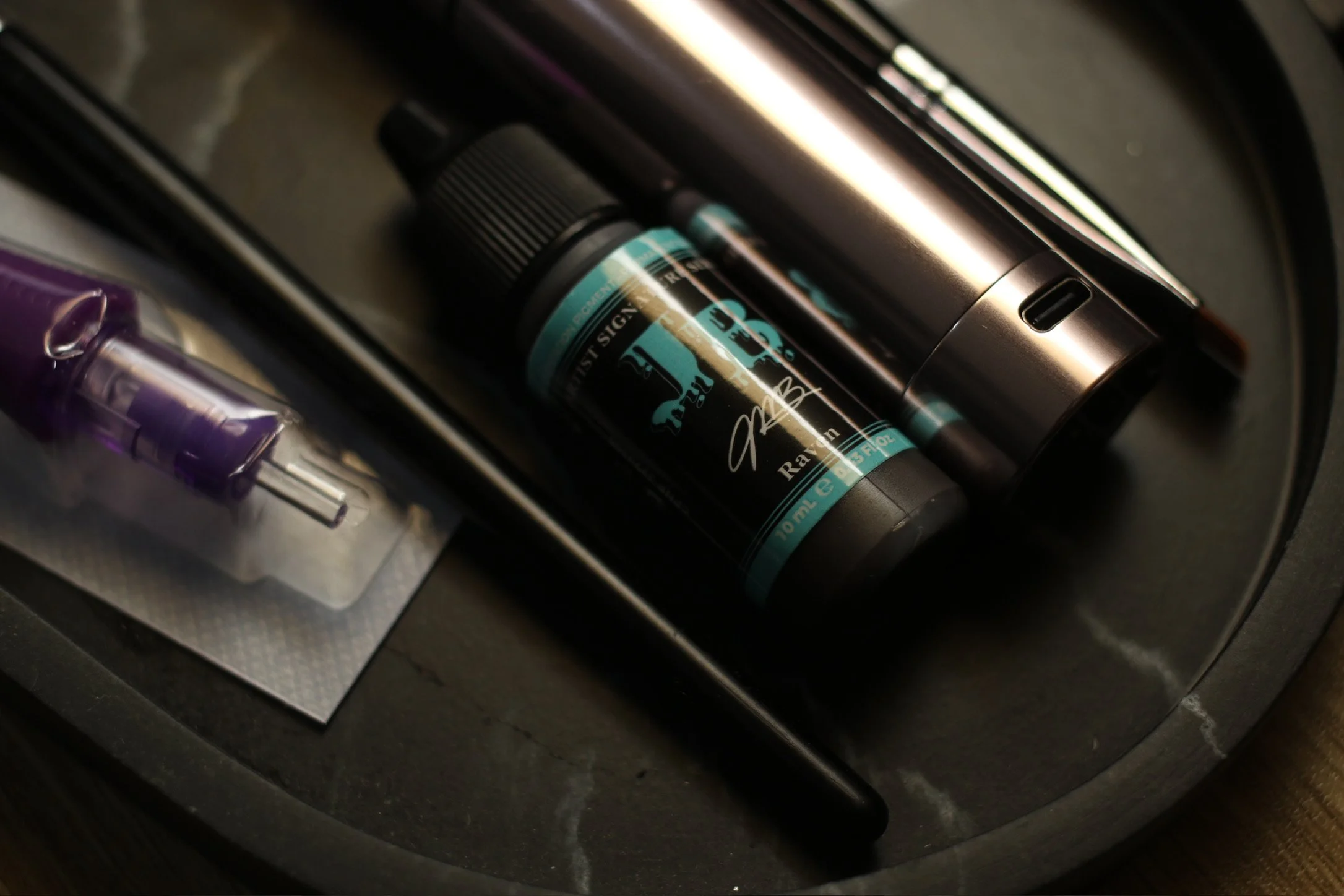 A tray with a small purple tattoo gun, a bottle of Ray RB e-liquid, a black eye dropper, and a tattoo gun.