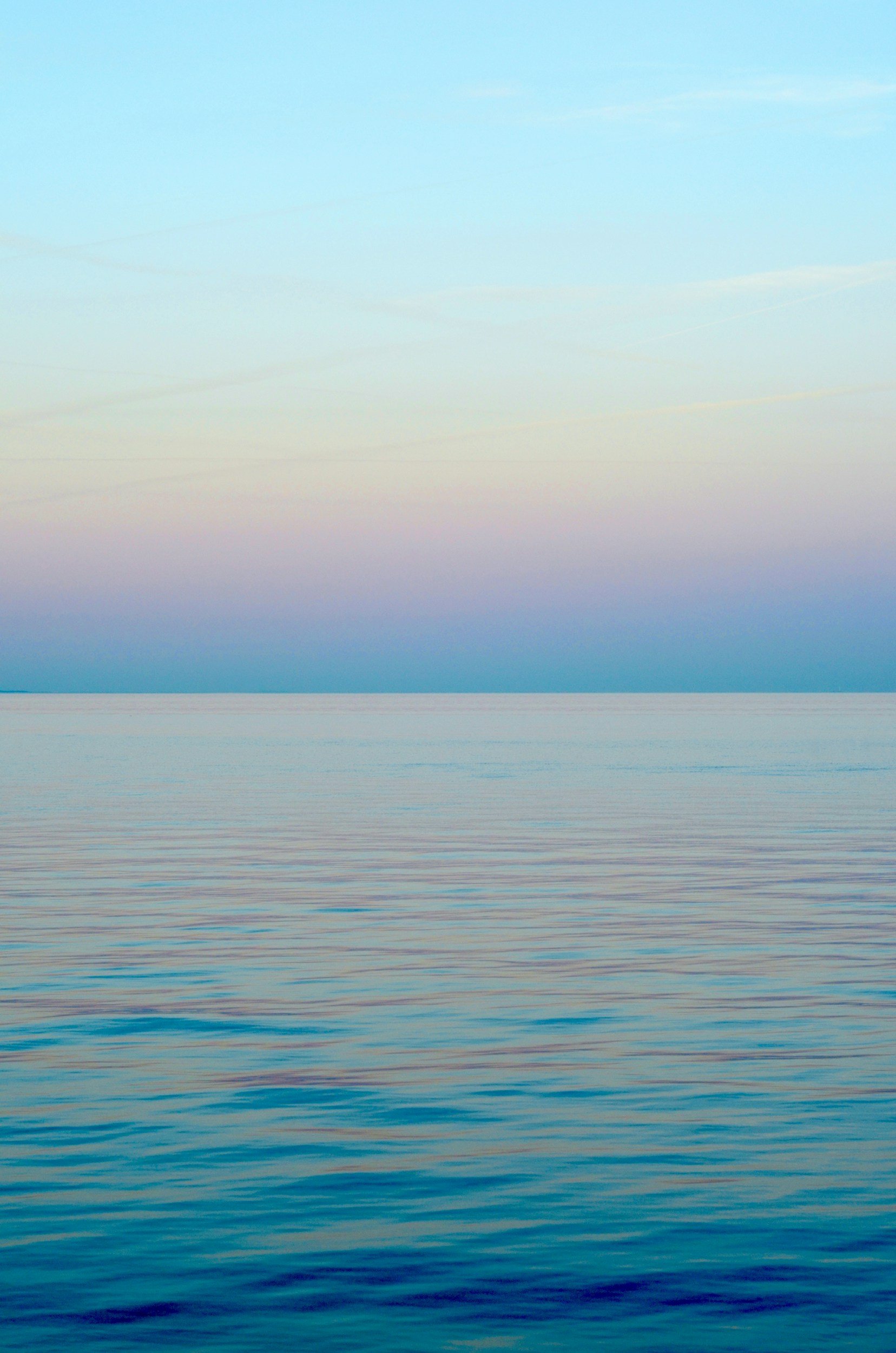 Calm ocean water with a gradient sky at sunset or sunrise, featuring soft pastel colors.