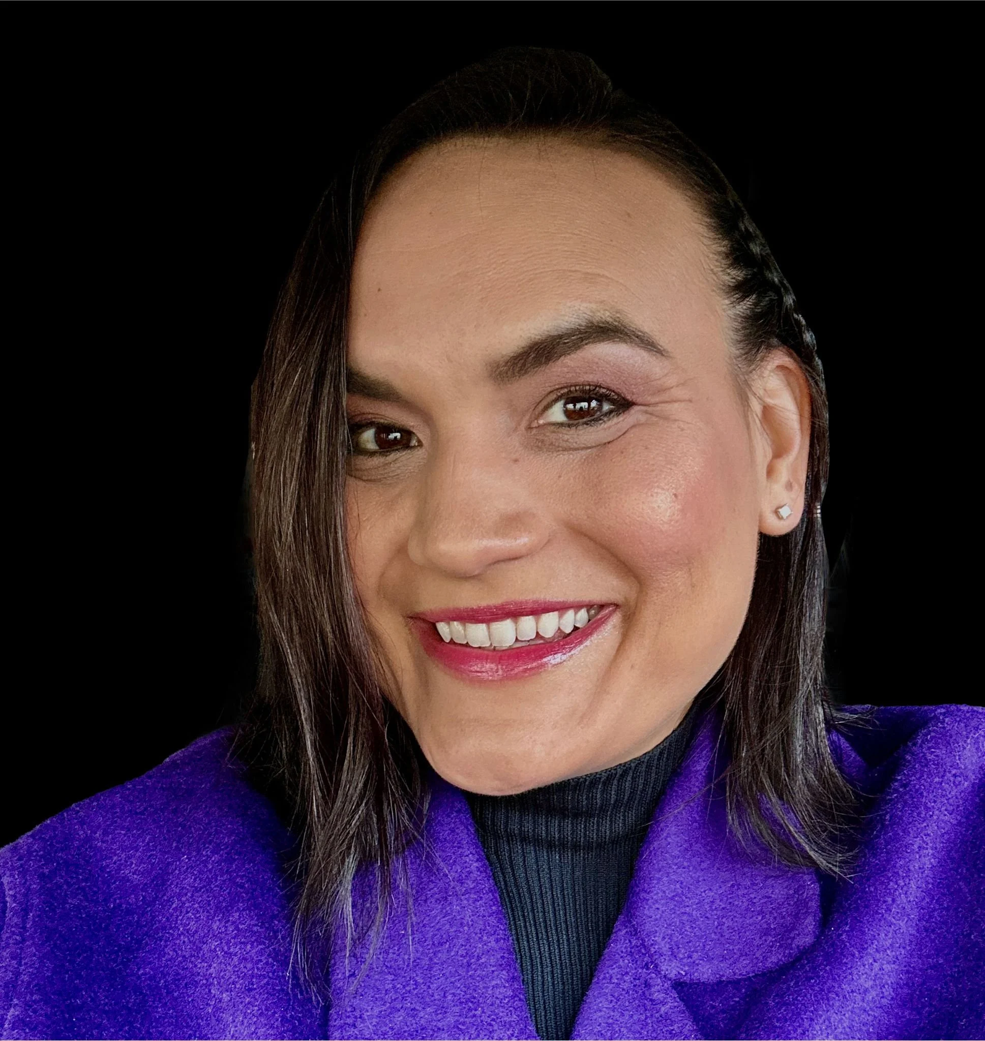 Close-up of a woman with dark brown hair, wearing a purple coat, smiling with white teeth, against a black background.