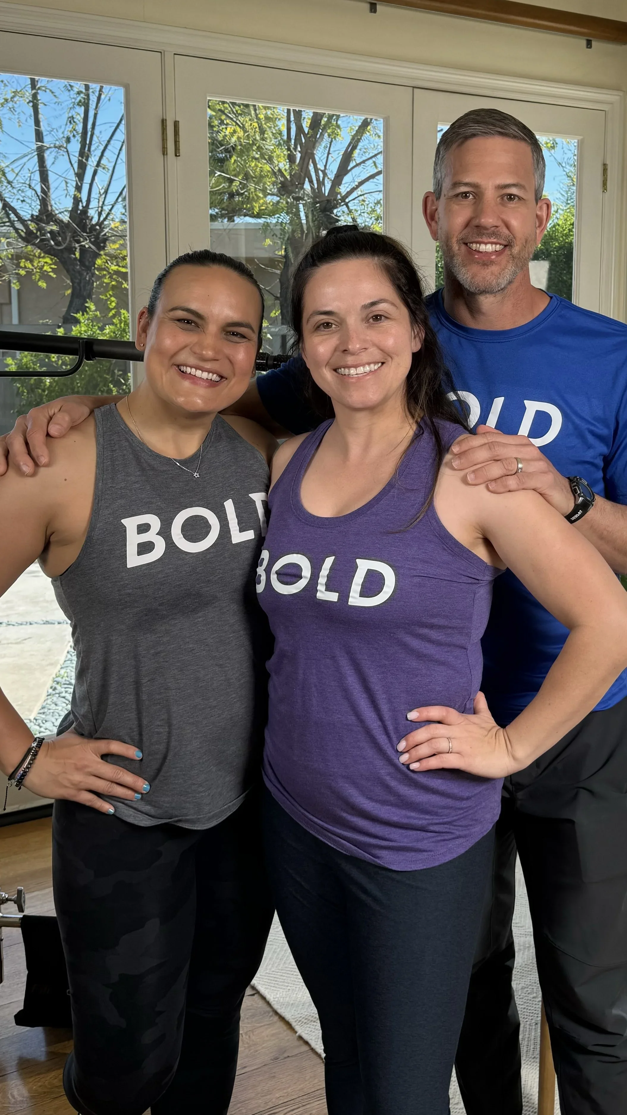 A smiling woman in a blue tank top pointing to the word 'BOLD' on her shirt, with a blue background and text including her name 'Melissa Kirkwood' and the title 'Bold Trainer'.
