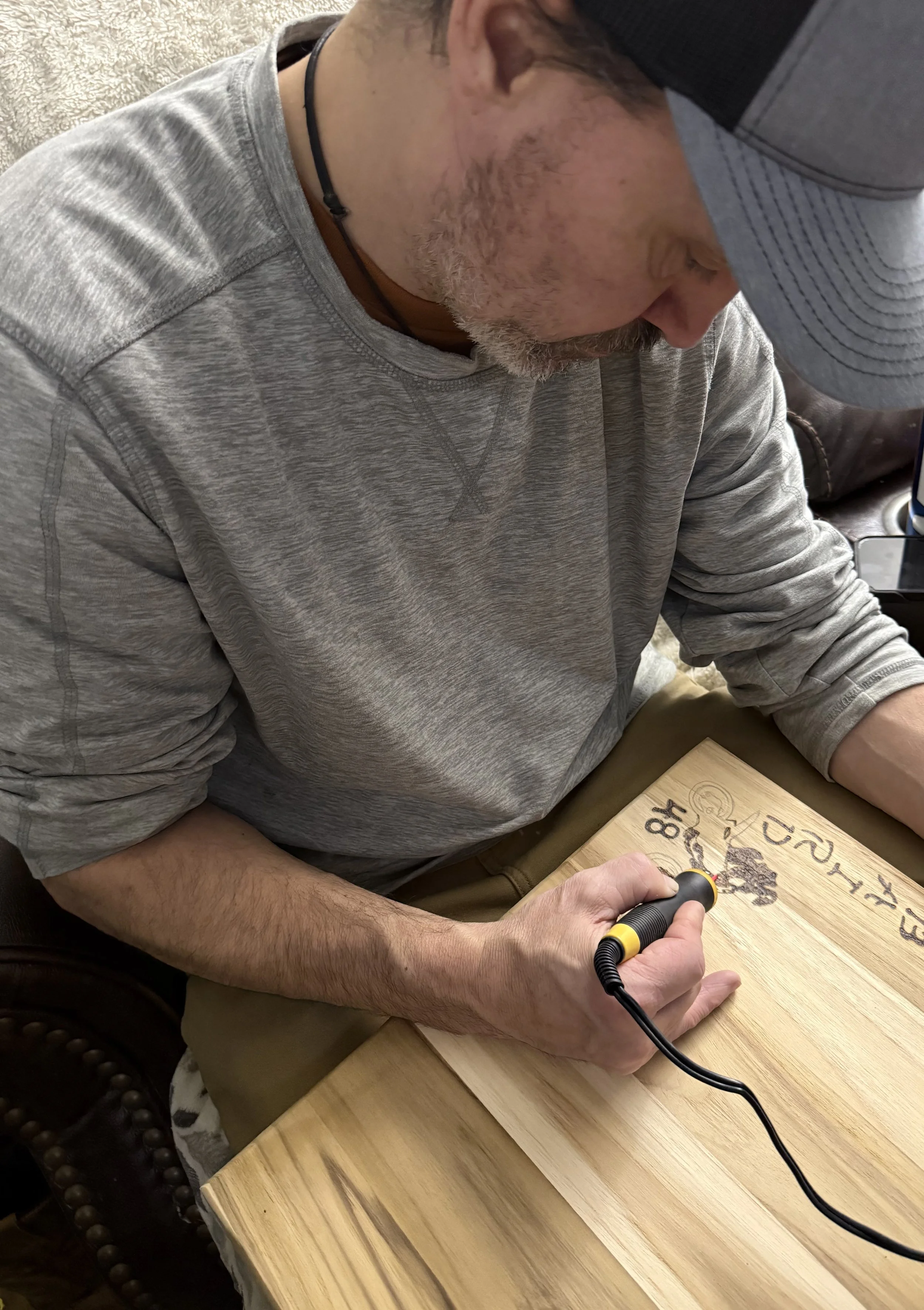 Rodney hand-burning a custom design into a wooden board, showing his handcrafted, by-hand woodworking process.