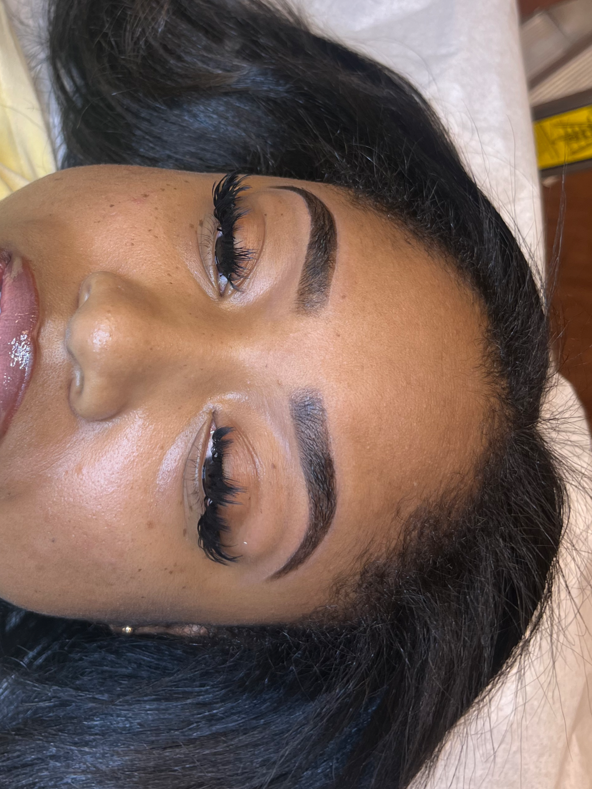 Close-up of a woman's face with well-groomed eyebrows and long eyelashes, lying down with her eyes closed.