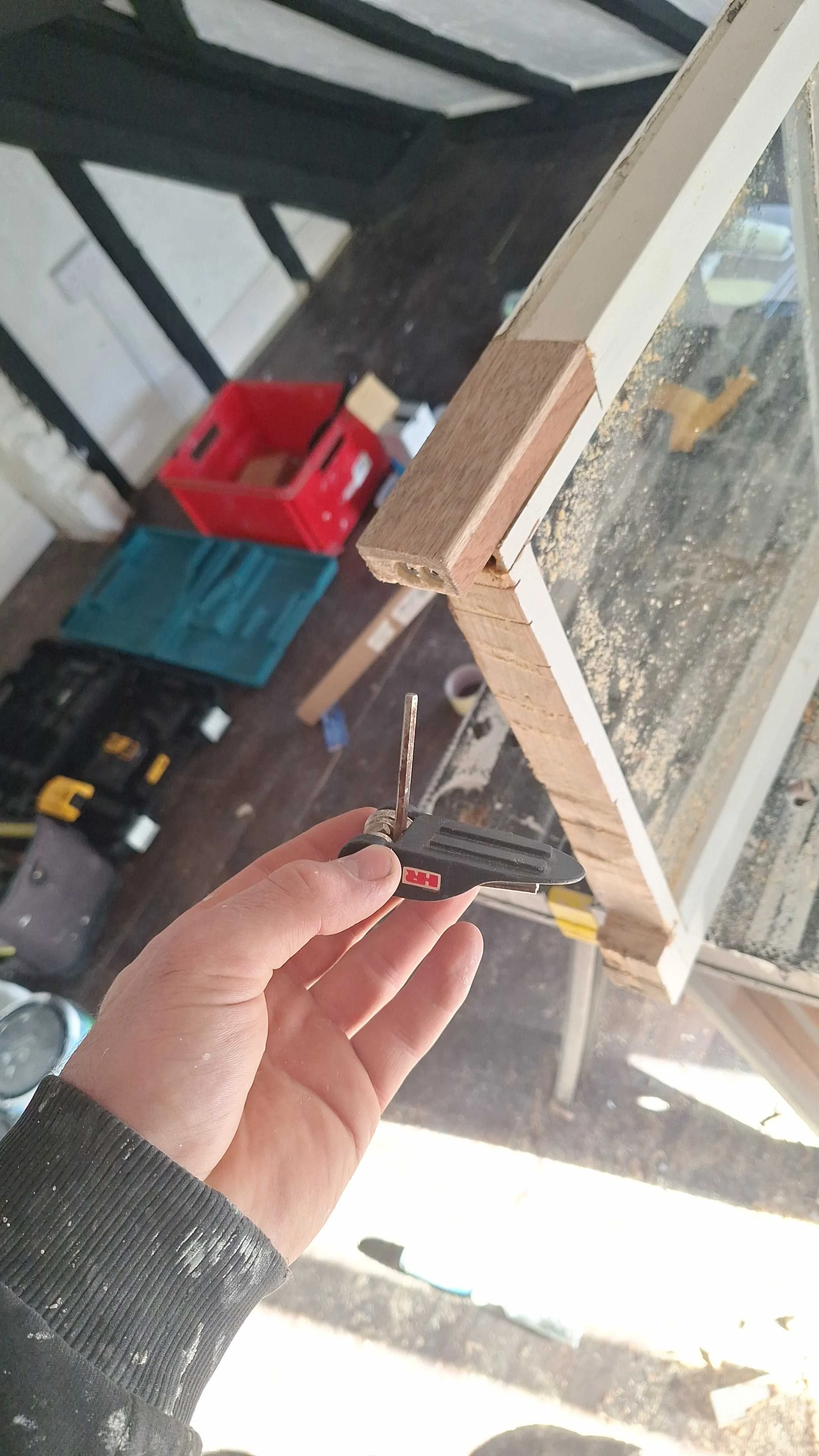 Close-up of a hand holding a small screwdriver, working on the corner of a wooden frame inside a workshop.