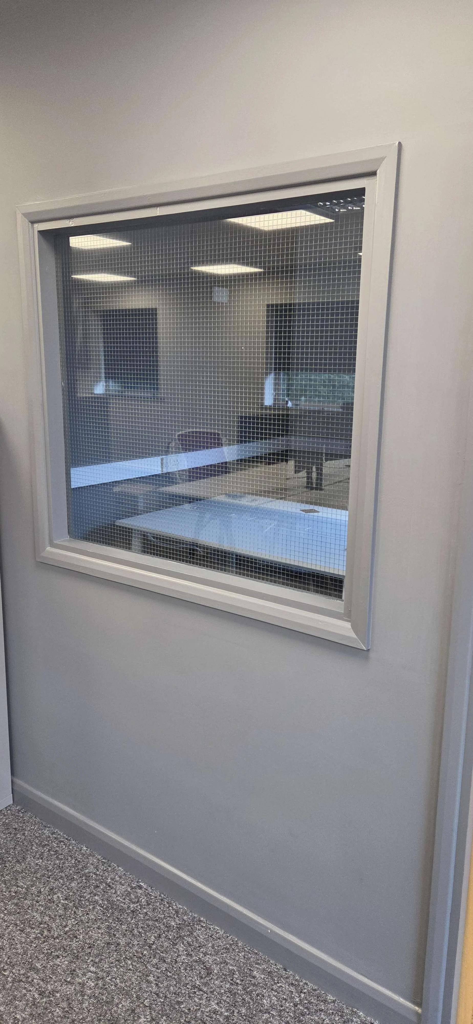 View through a glass window with wire mesh installed in a room with a table and chairs, office environment