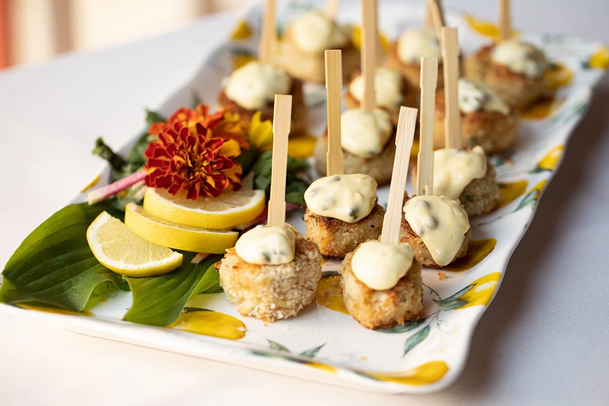 Crispy bite-sized appetizers topped with creamy sauce, garnished with lemon slices and flowers on a decorative platter.