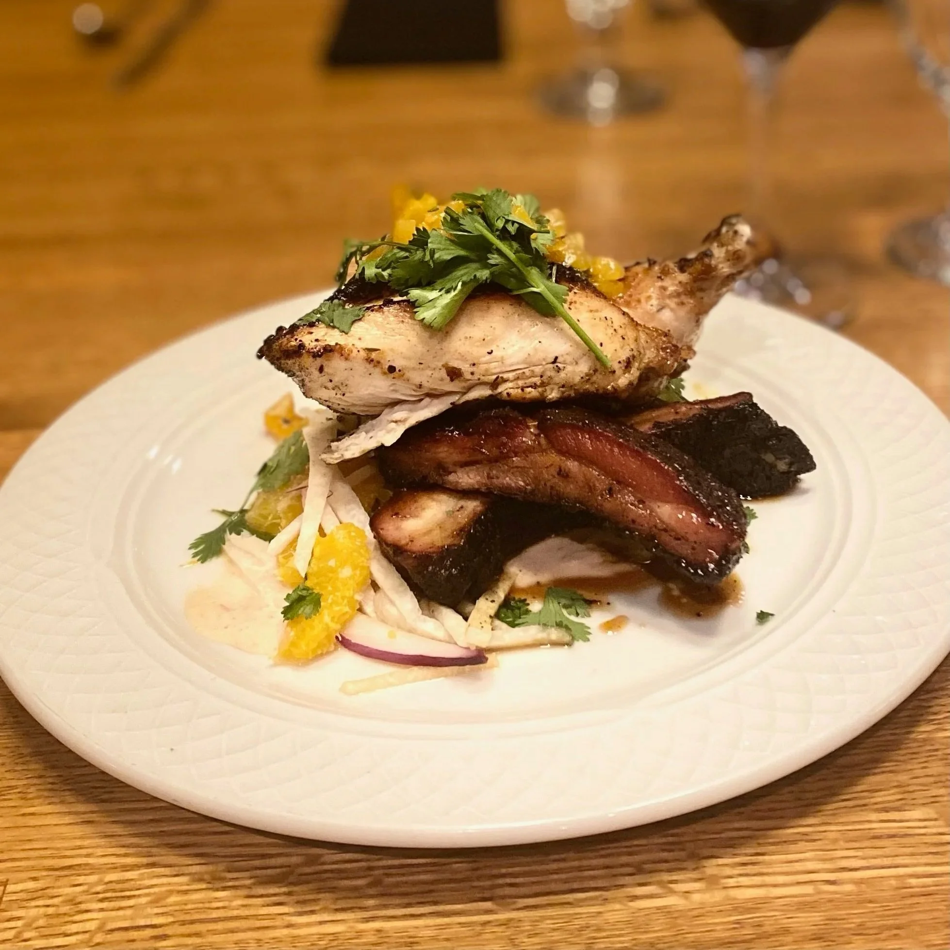 Plate of grilled chicken, pork ribs, and fresh salad garnished with cilantro and orange zest, served on a white plate with a wooden table background.