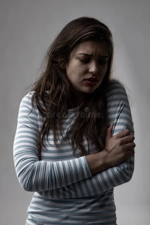 A woman with long brown hair wearing a striped long sleeve shirt, appears to be upset or in pain, holding her left arm with her right hand.