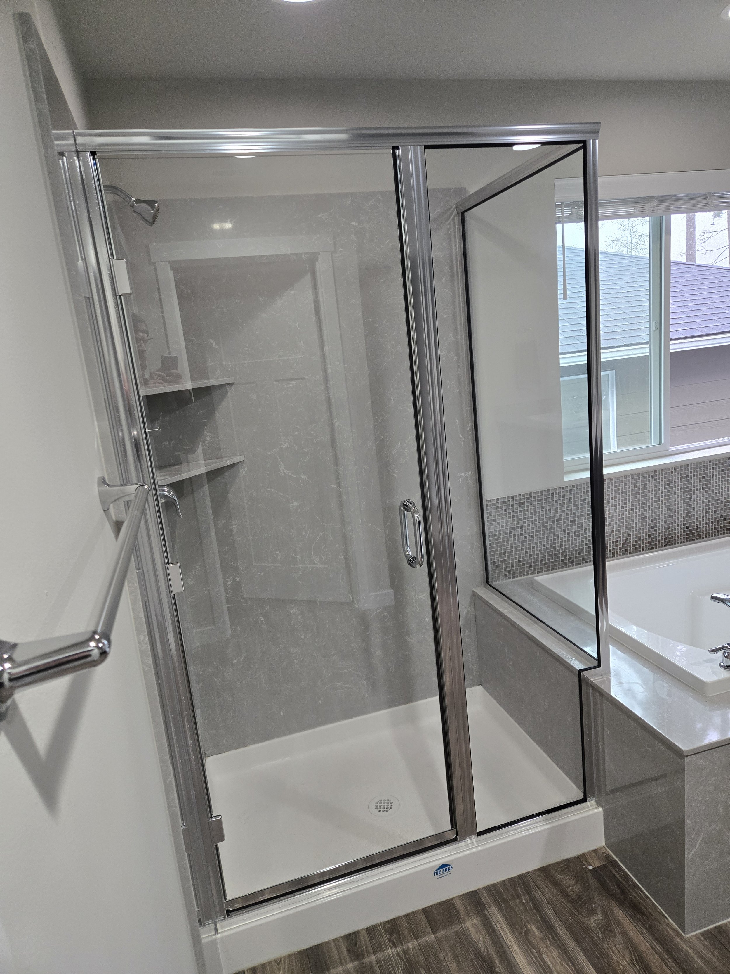 A modern bathroom with a glass shower enclosure, marble walls, and a bathtub with a window above it.