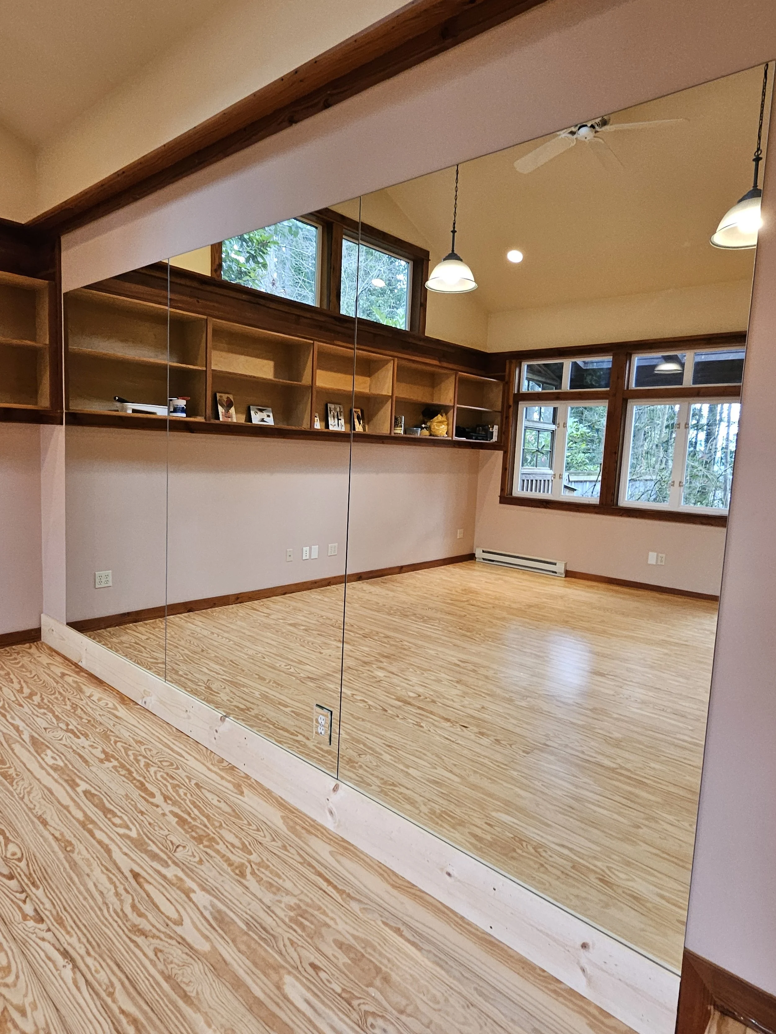 Empty room with large mirror, wooden trim, built-in shelves, hardwood flooring, multiple windows, ceiling fan, and hanging lights.