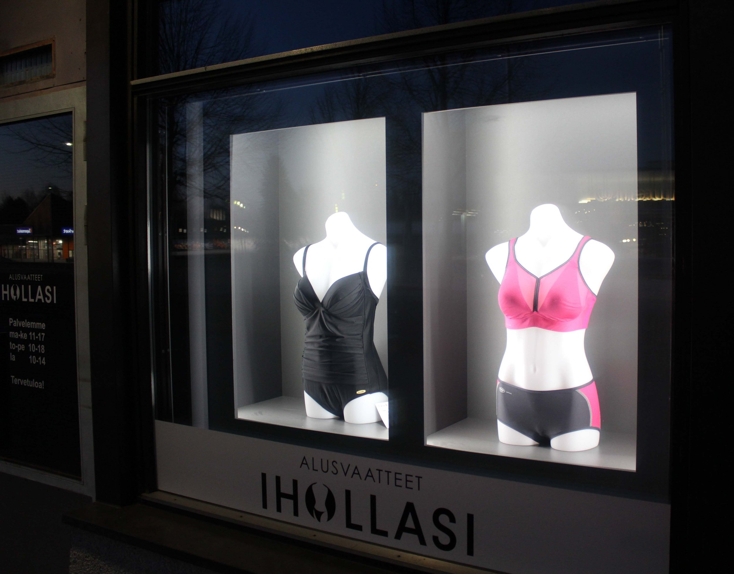 Näyteikkuna ulkoapäin. Kaksi  mallinukkea puettuna ja valaistuna.