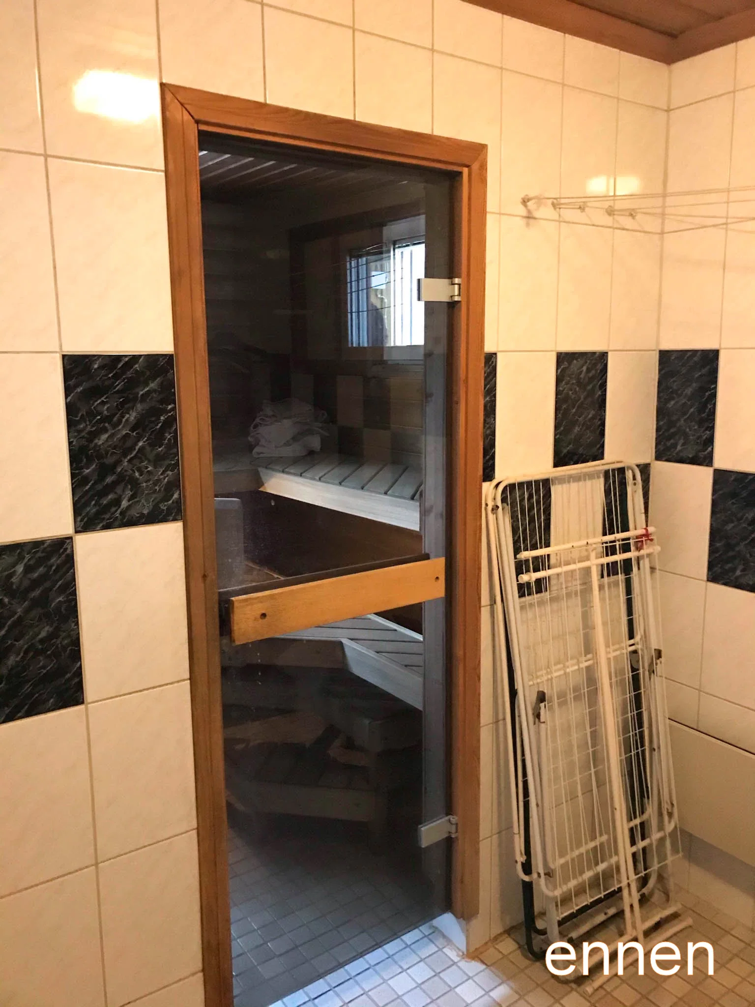 Kuva kylpyhuoneen saunasta, jossa on lasiovi ja puinen ulkoasu, sekä pyykinkuivausteline.