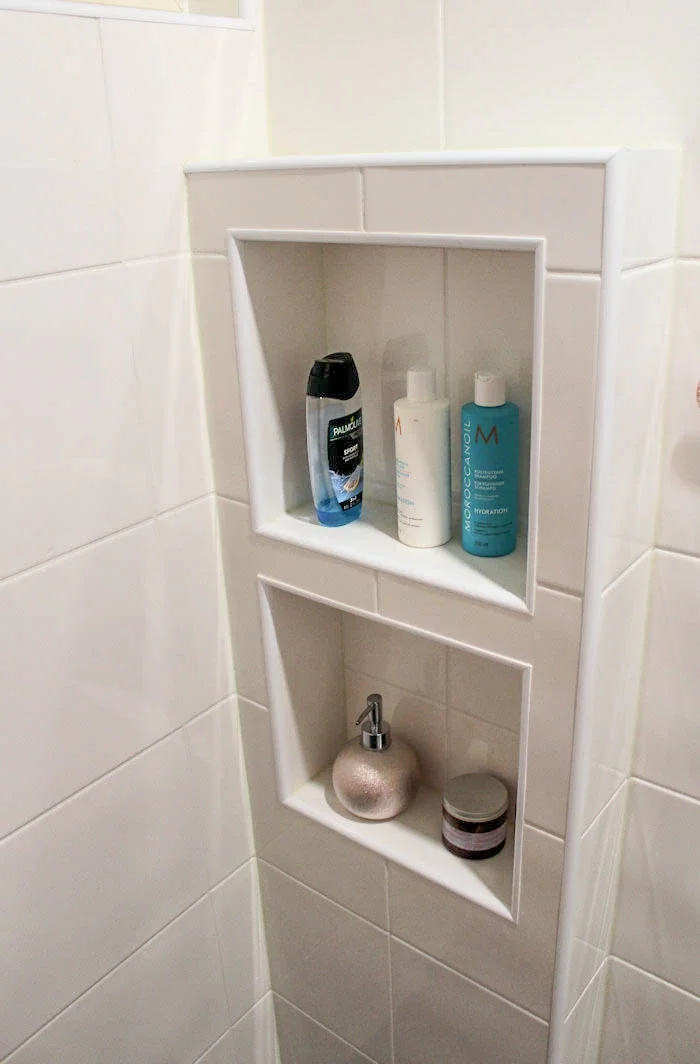 Kaksi päällekkäistä kylpytarvikehyllyä, joissa kosmetiikkatuotteita kuten shampoota, hoitoainetta ja pesunesteitä.