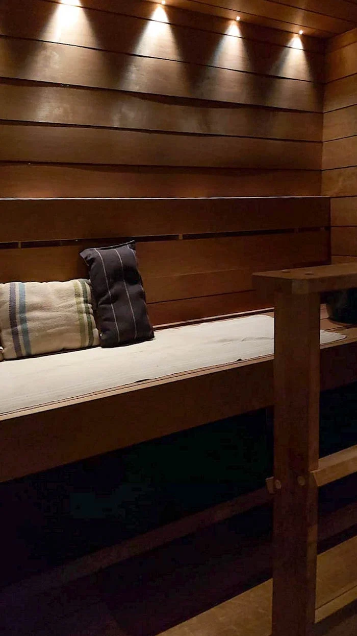 Sauna, jossa valaistus tulee keilamaisena takaseinään. Lauteella laudeliinat.