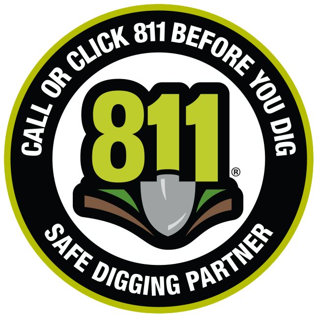 A circular safety badge with a black outer ring and a green inner border. The text on the badge reads "CALL OR CLICK 811 BEFORE YOU DIG" at the top and "SAFE DIGGING PARTNER" at the bottom. In the center, there is a graphic of a shovel embedded in the ground with the number "811" in large green font.