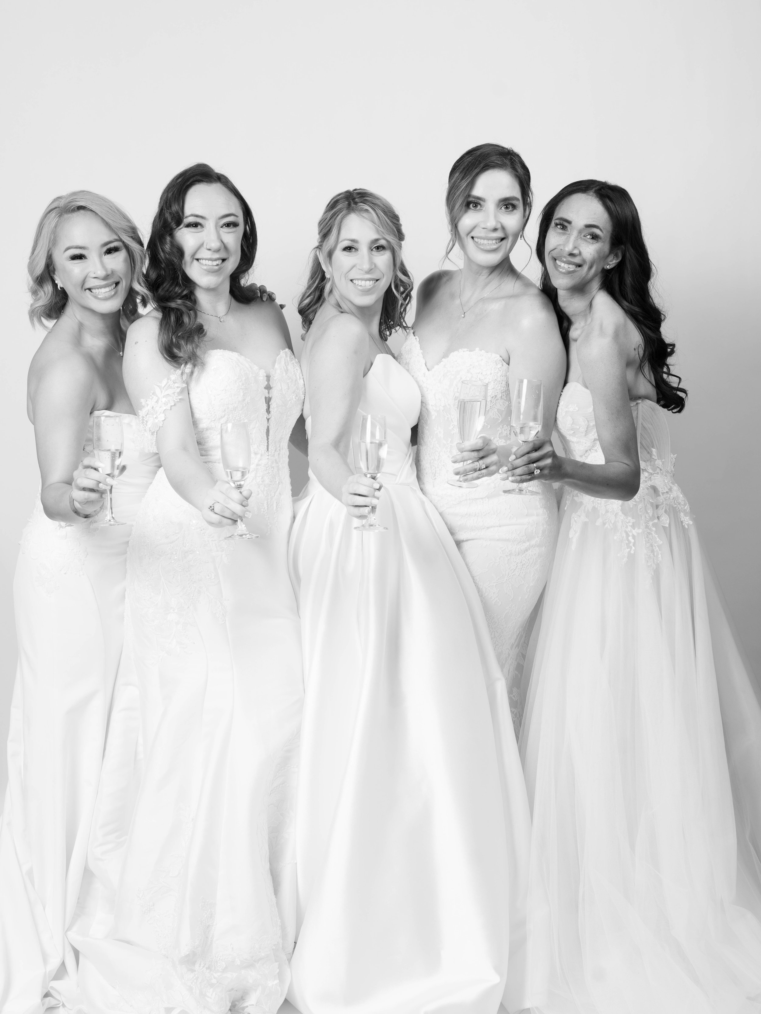 Women in wedding dresses celebrating with glasses of champagne.
