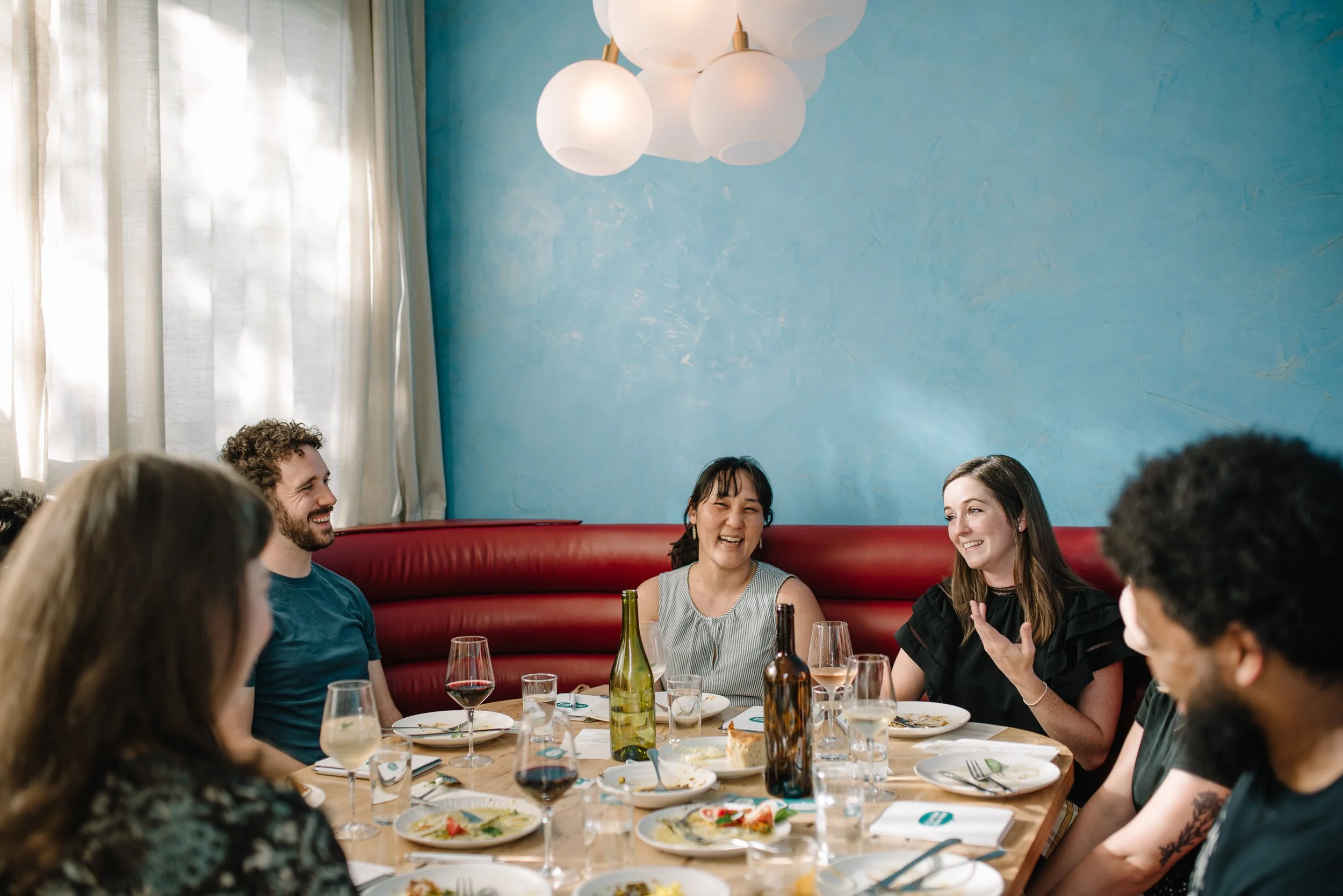 A group of people sitting at a long dinner table in a warmt, modern space.