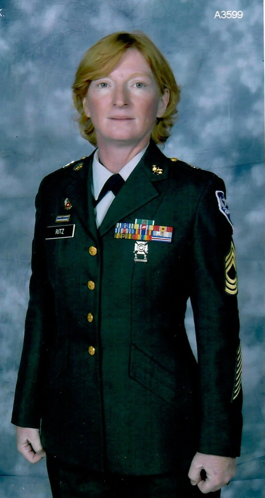 A woman in a military uniform with medals and ribbons, standing against a gray background.