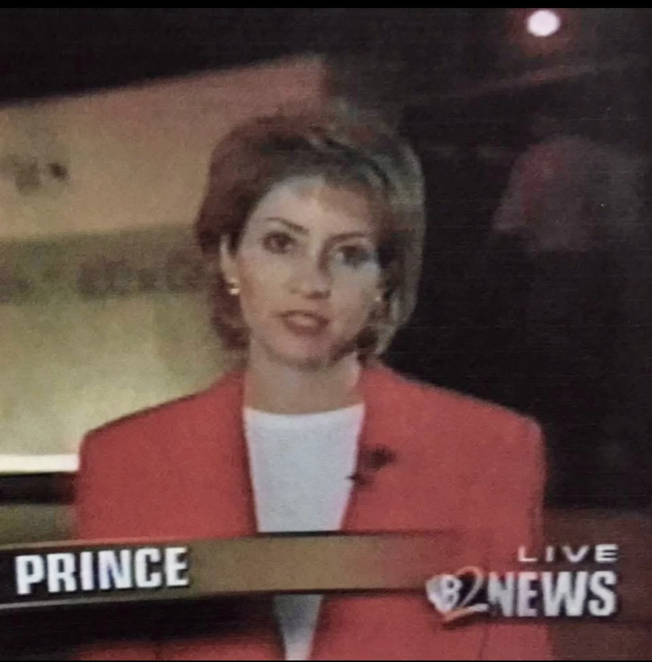 Julie wearing a red blazer and white top, speaking into a microphone on a TV news broadcast with the text 'PRINCE' and 'LIVE 2 NEWS' at the bottom.