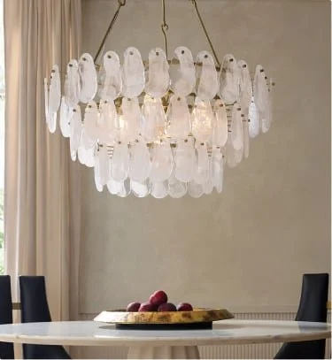 A modern chandelier with multiple white, teardrop-shaped glass ornaments hanging above a dining table with a bowl of red apples.