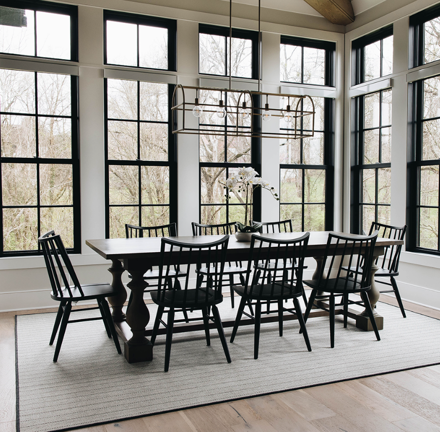 Dining room with large windows, black chairs, a wooden table, and a modern chandelier.