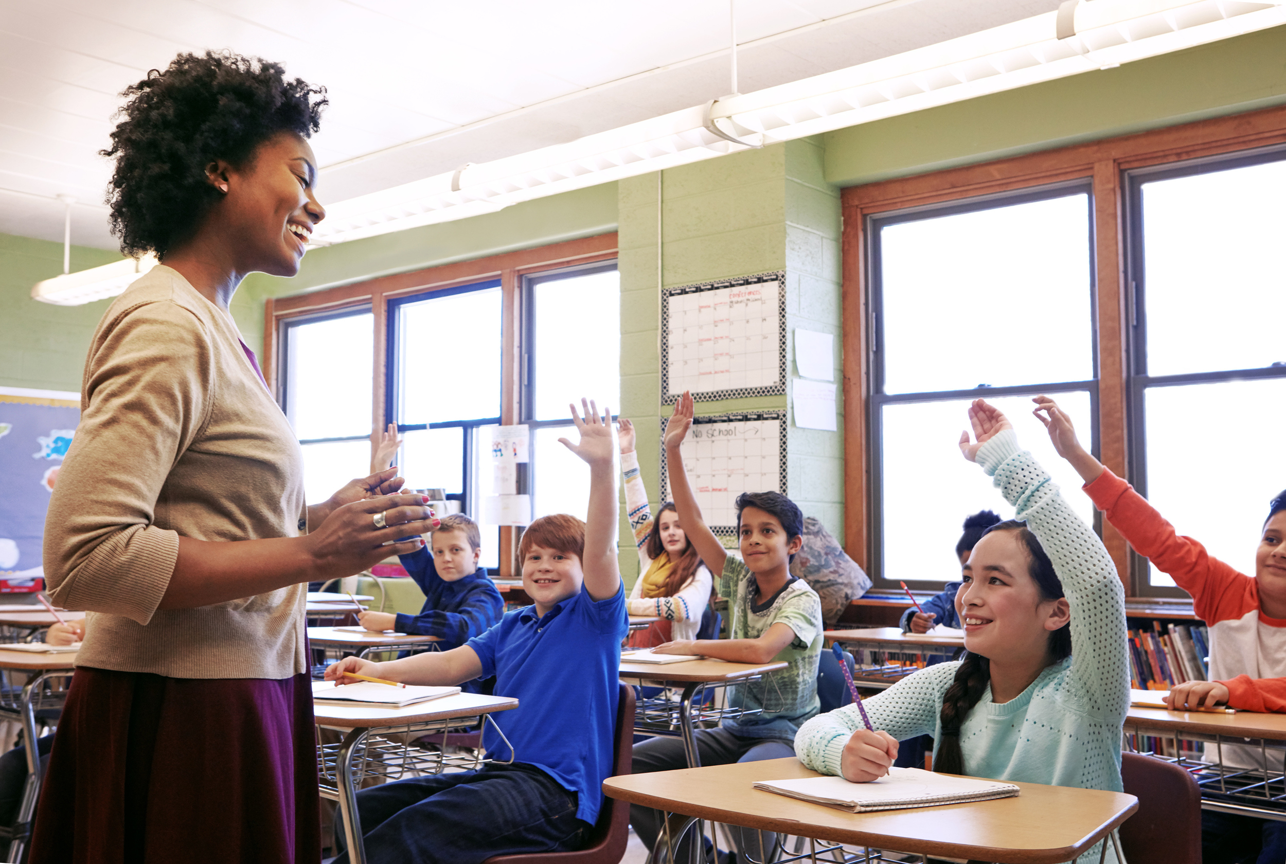 A teacher in a classroom with students raising their hands during class.