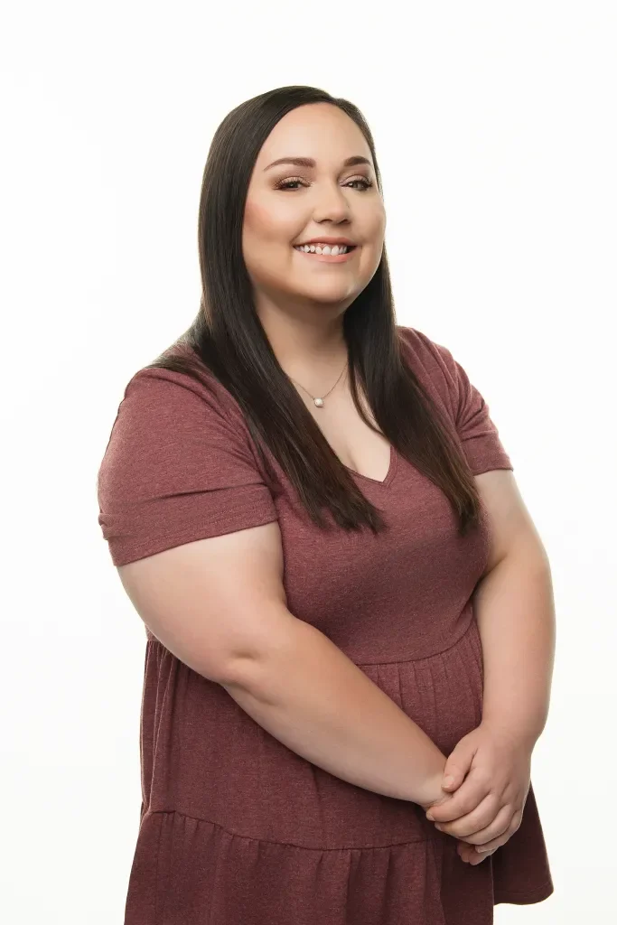 A smiling woman with long dark hair wearing a maroon dress against a white background.