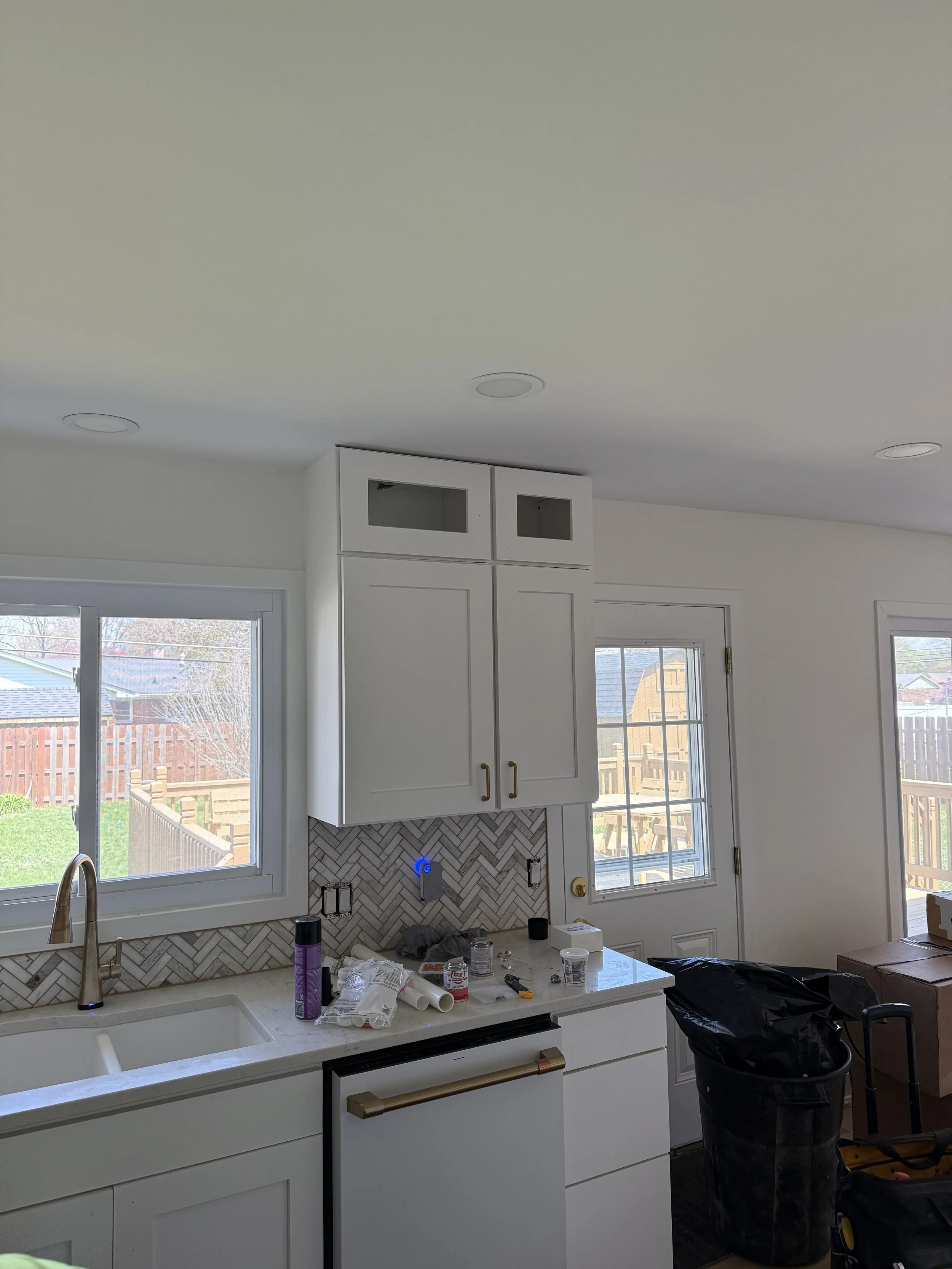 Kitchen with white cabinets, a white countertop, two windows, a black trash can, and new appliances and tools on the counter indicating ongoing renovation.