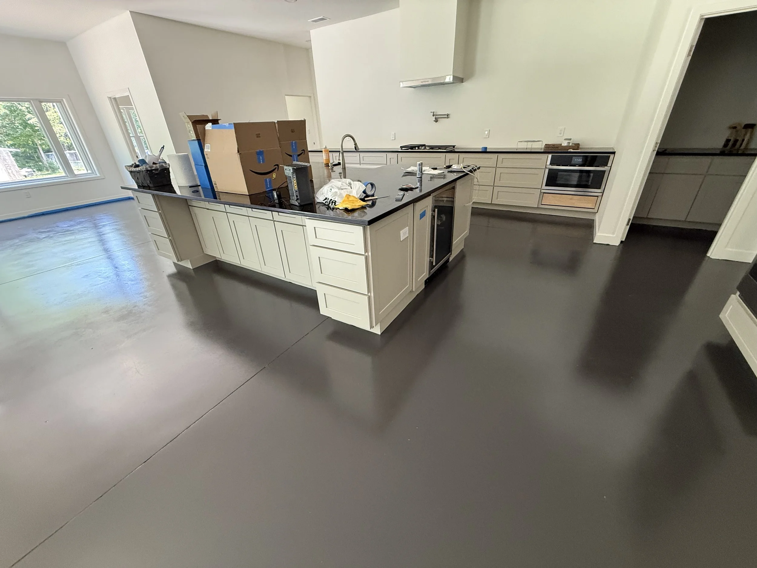 A kitchen under construction with a large island, white cabinets, built-in appliances, and a dark polished concrete floor.