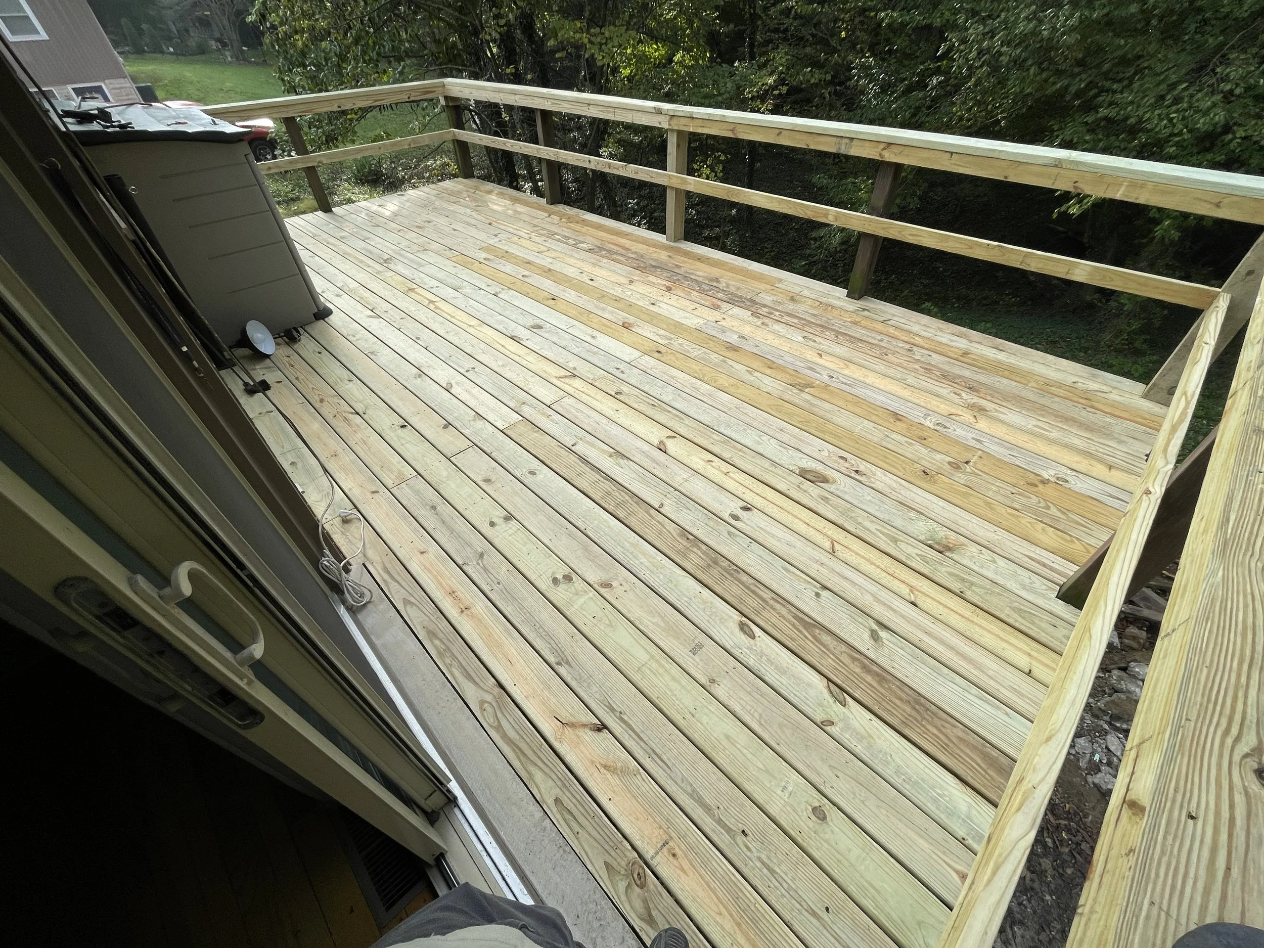Newly built wooden deck extending from the house, with partial railing and outdoor grill, overlooking a grassy yard with trees.