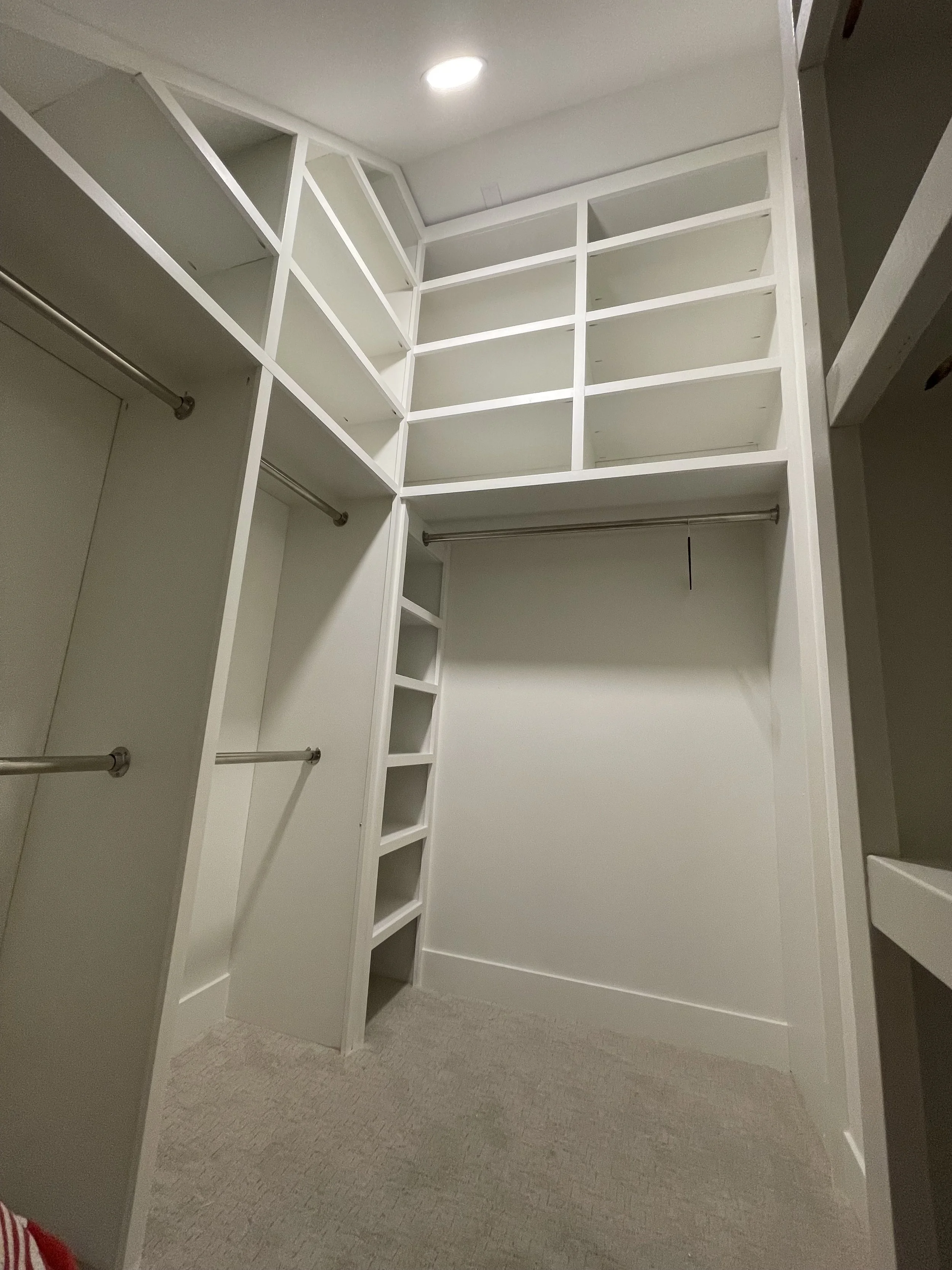 Empty walk-in closet with white shelving, hanging rods, and beige carpet.
