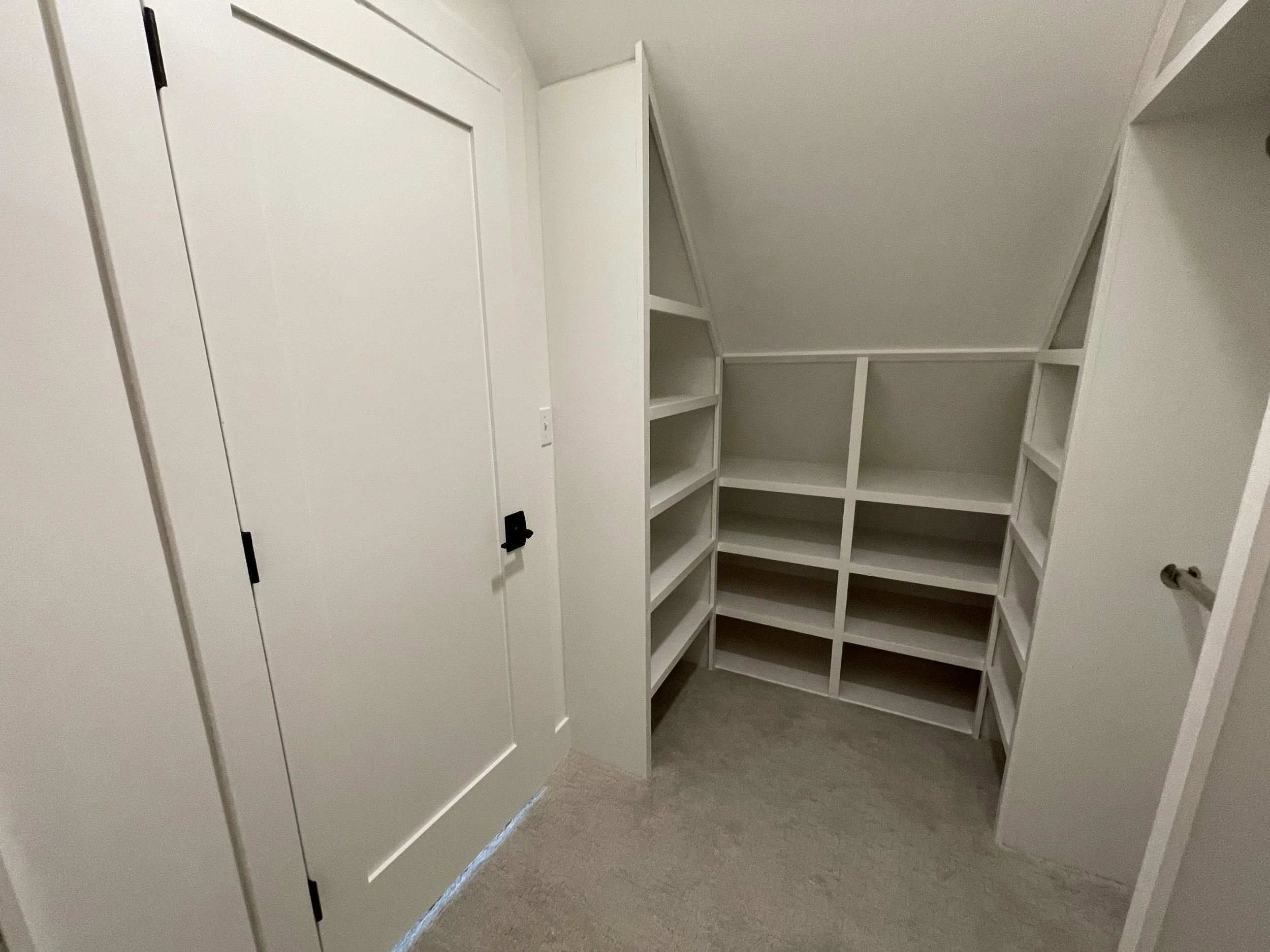 Empty closet with white built-in shelves and a sloped ceiling.