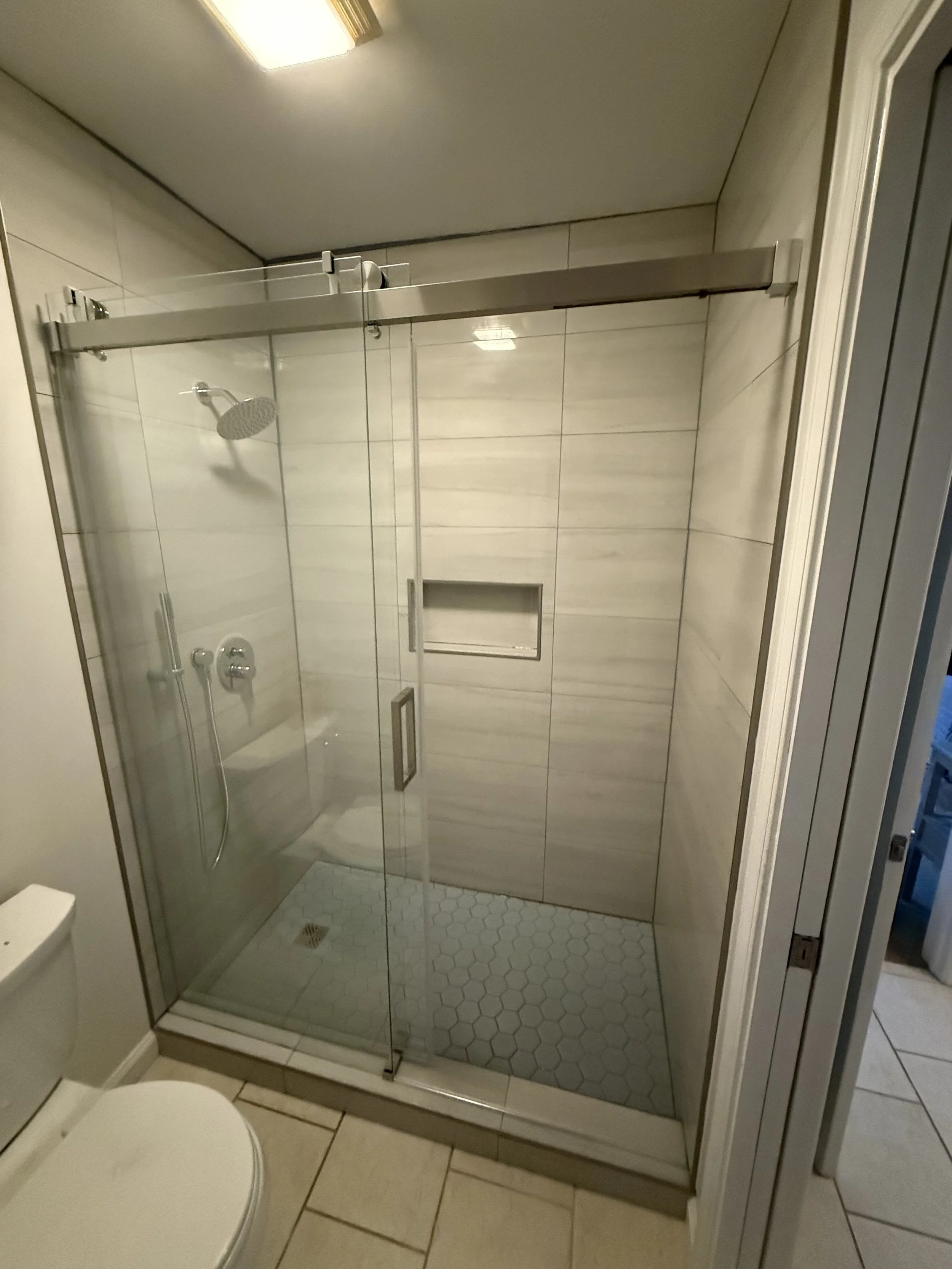 Bathroom with walk-in glass shower enclosure, tiled walls, and a small built-in shelf in the shower area.