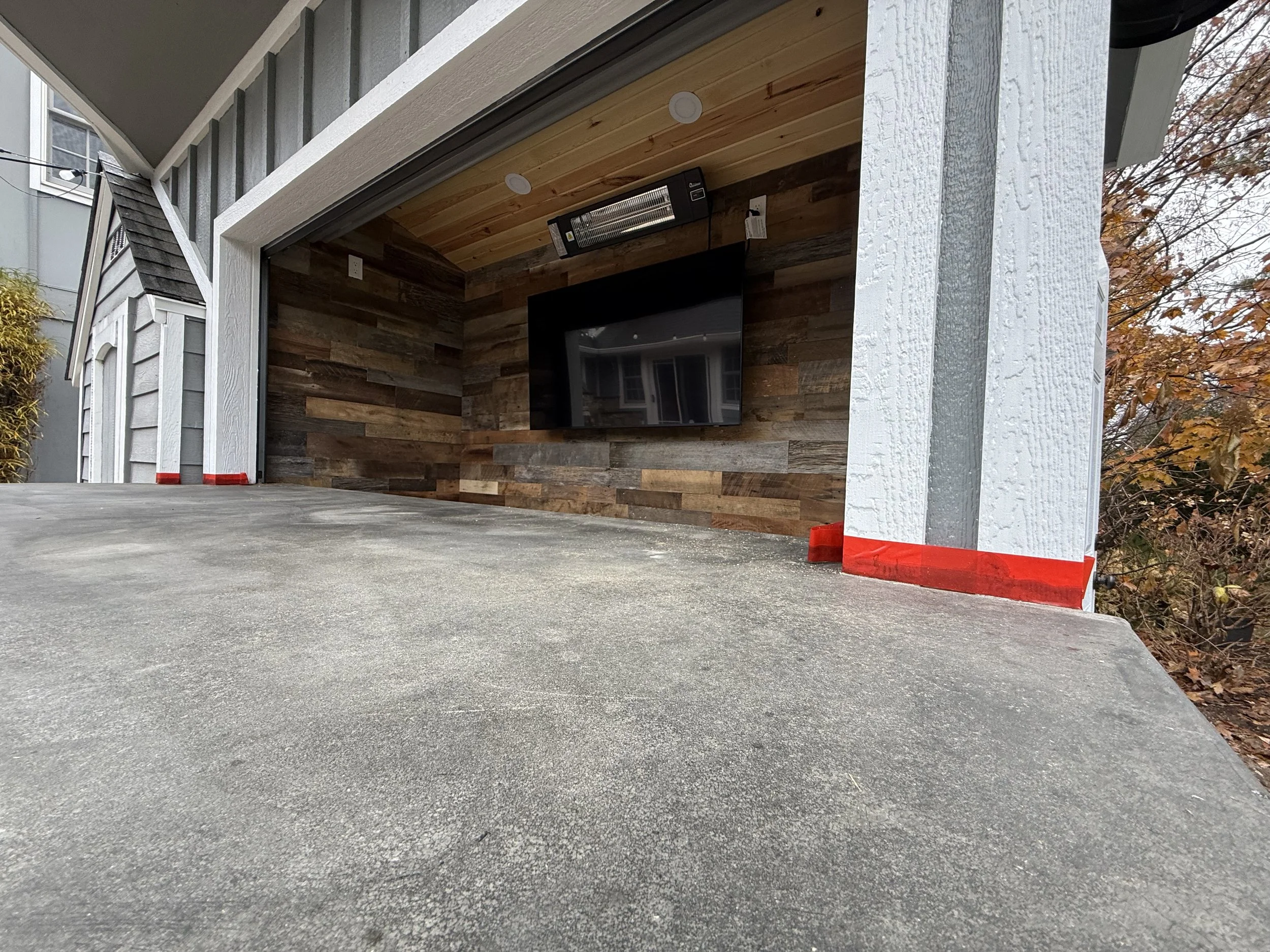 View of a garage with a concrete floor, white textured wooden beams, a wall with wood paneling, and a flat-screen TV mounted on the wall.