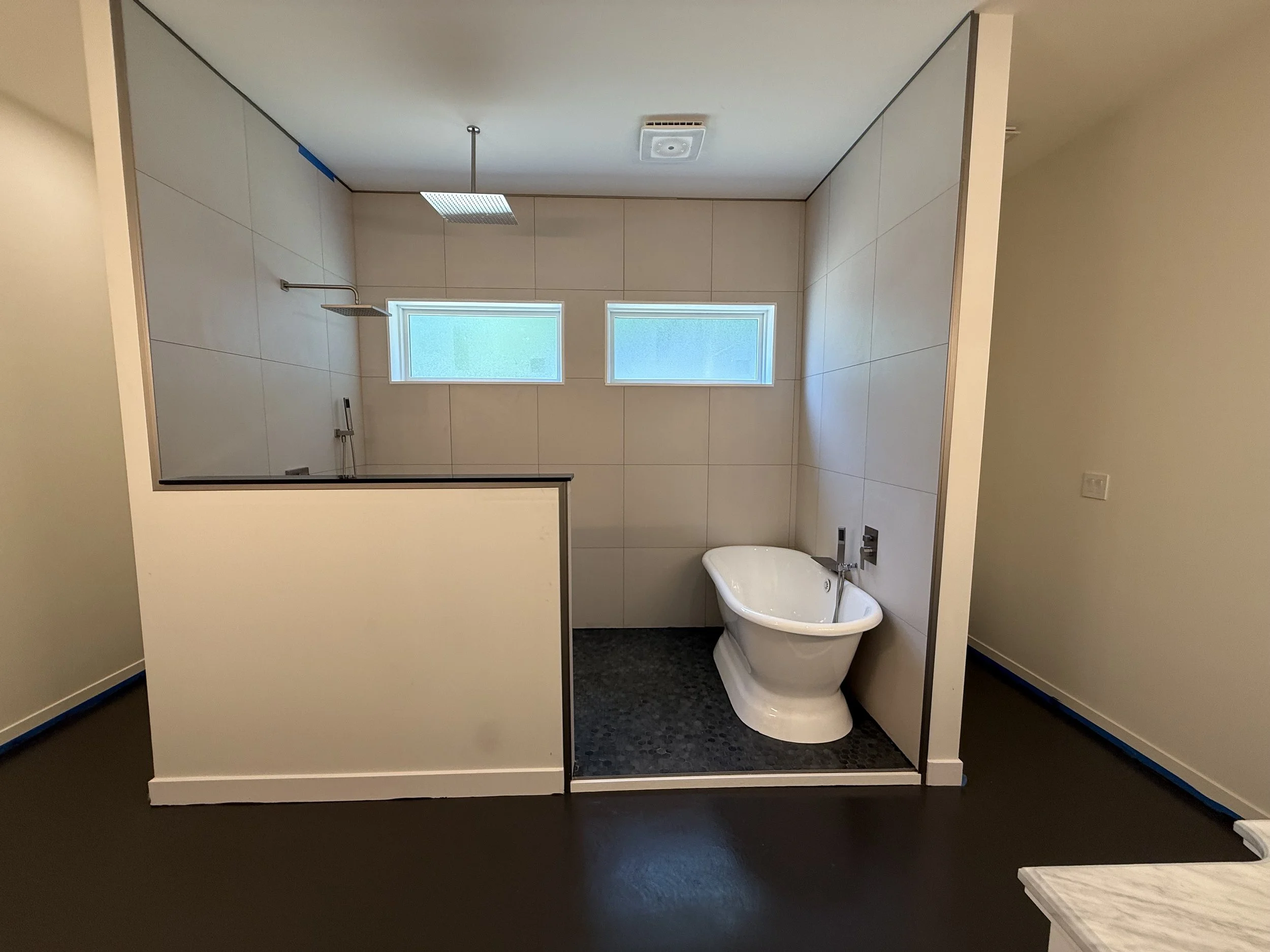 A modern bathroom featuring a glass-enclosed shower area with two small horizontal windows and a freestanding bathtub on black tiled flooring.