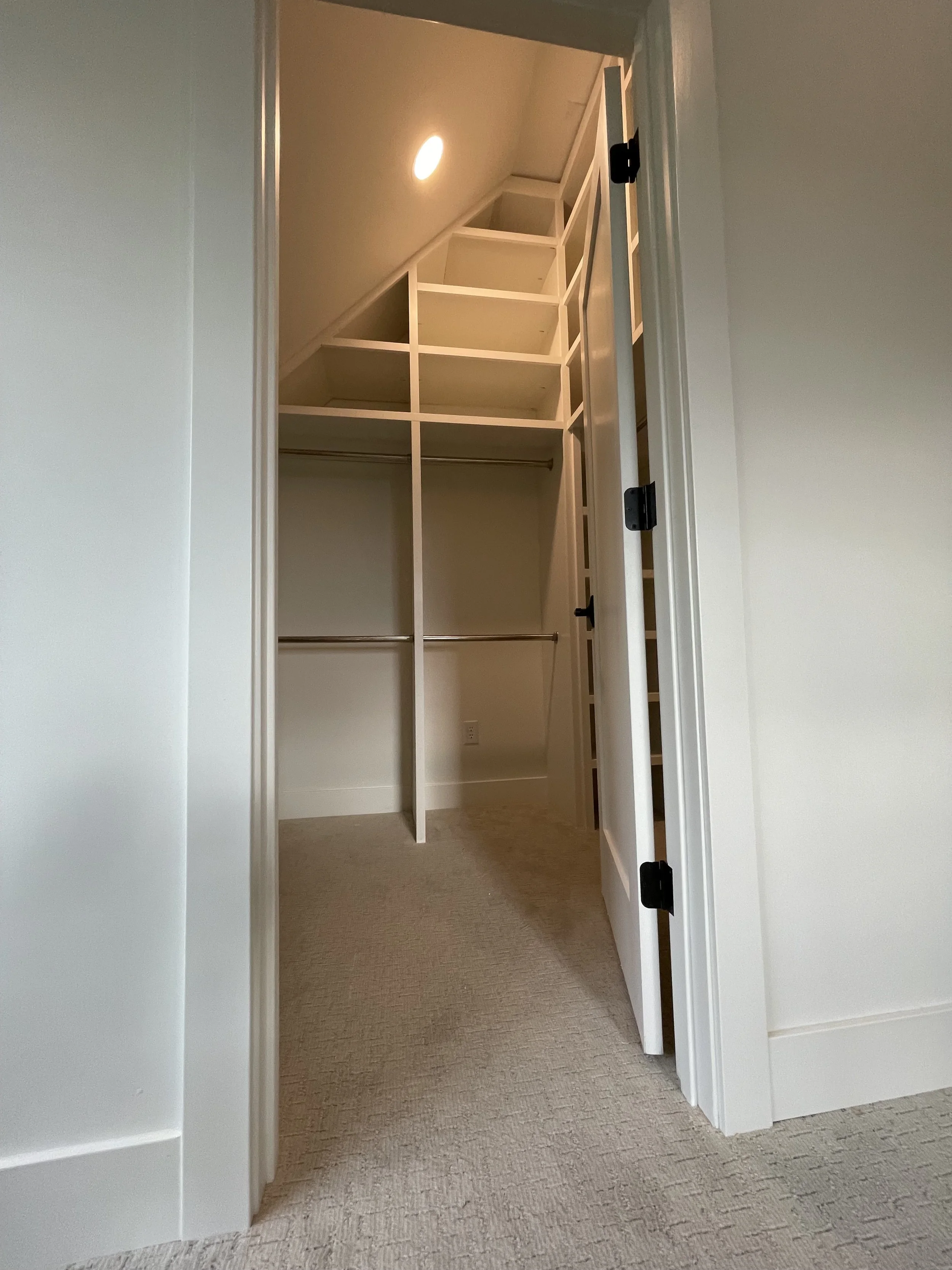 Empty walk-in closet with built-in shelves and hanging rods, viewed through an open door.