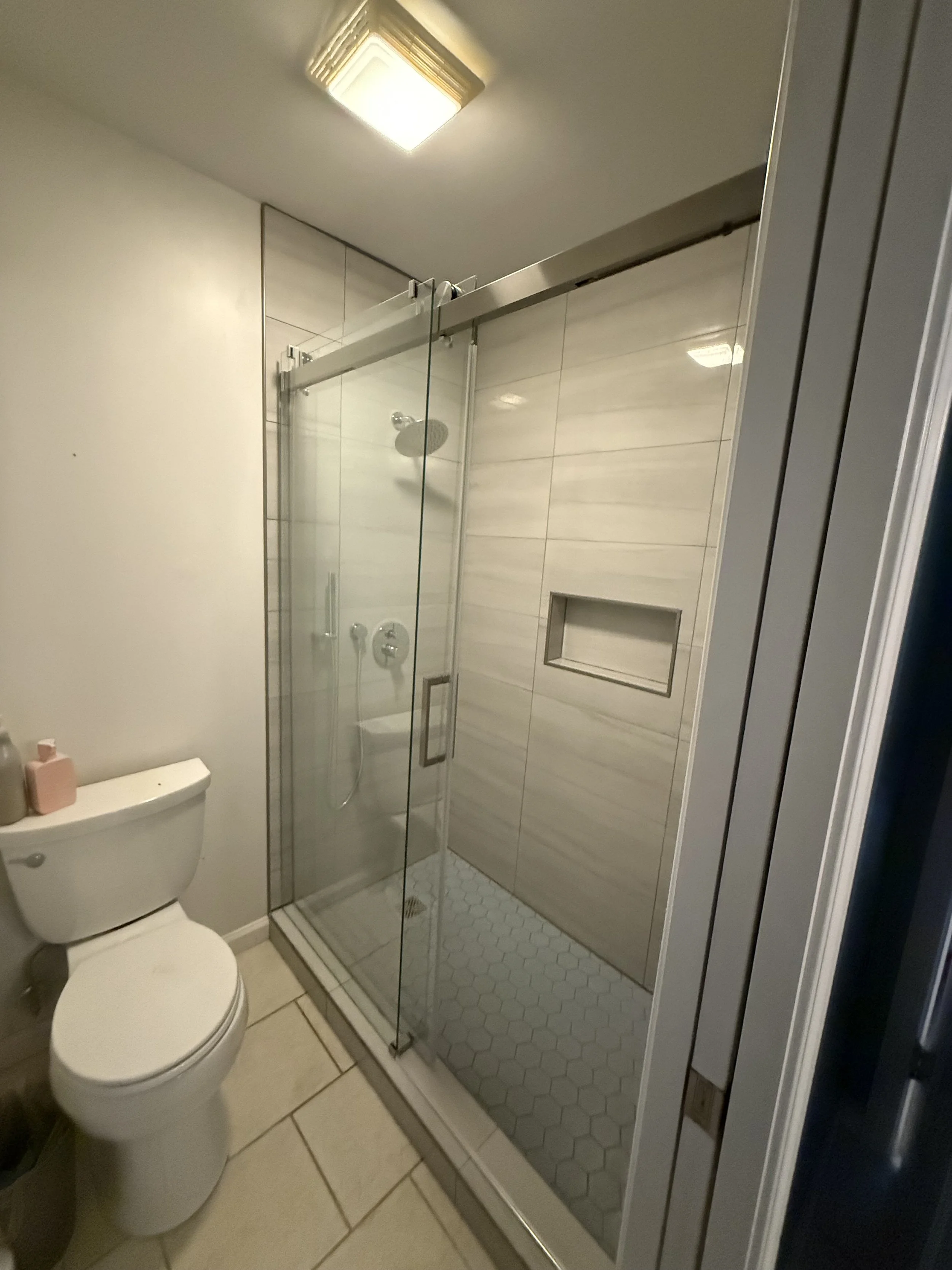 Bathroom with a glass shower enclosure, a white toilet, and beige floor tiles.