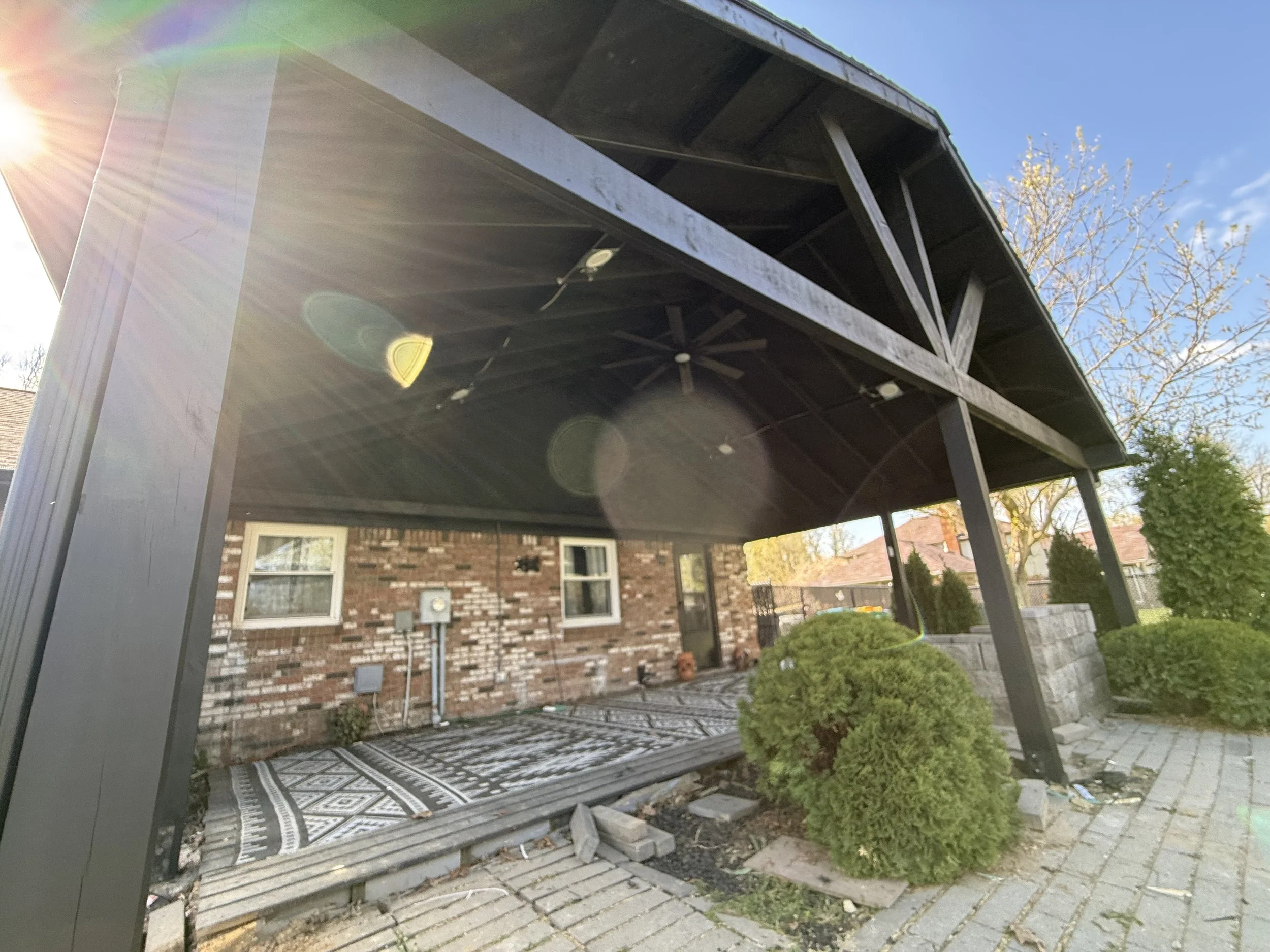 Backyard patio with a covered pergola, brick house in the background, and neatly trimmed bushes.