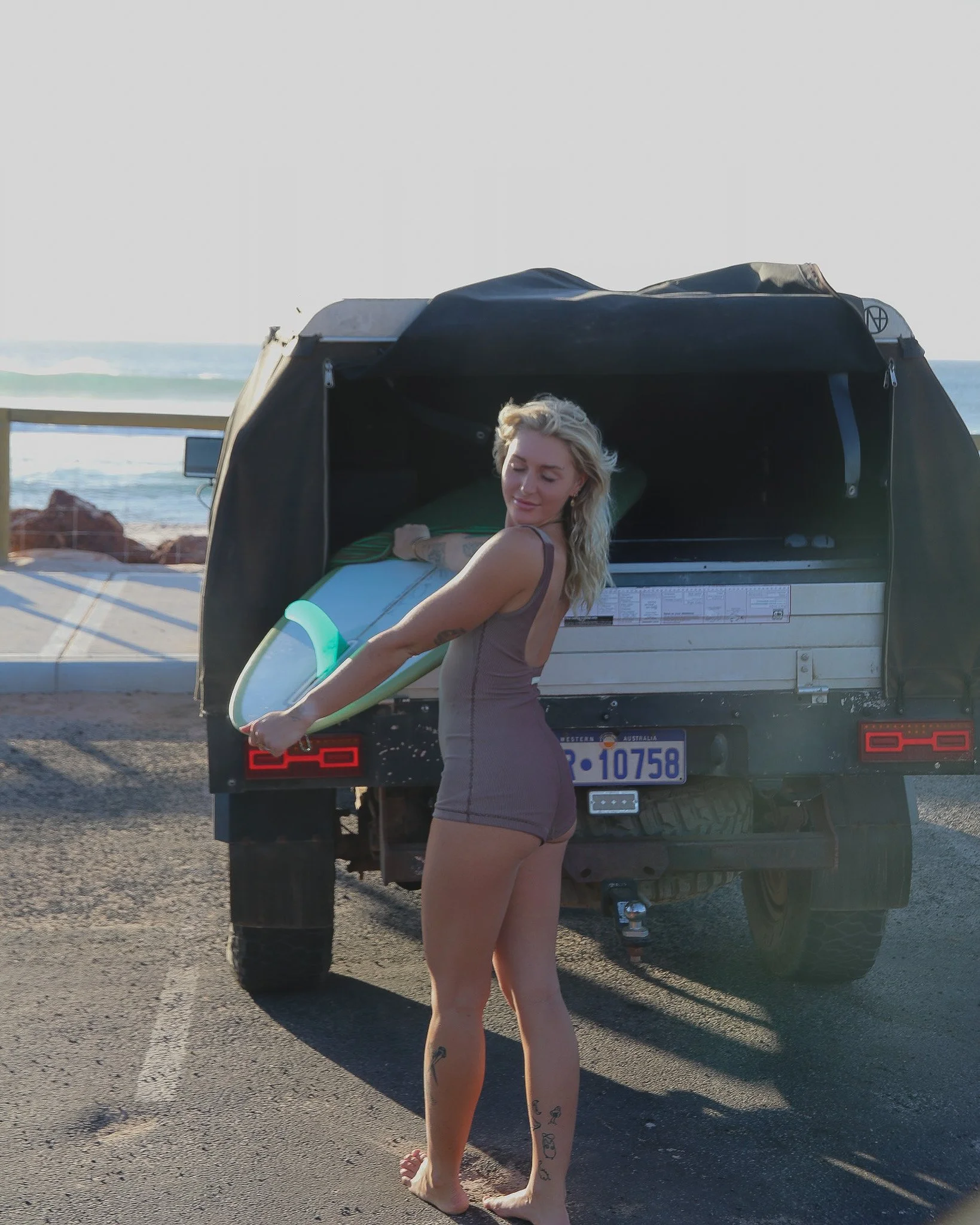Woman in swimsuit carrying a surfboard near a parked truck at the beach.
