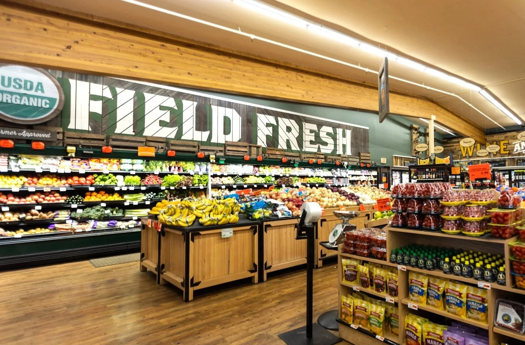 Fresh produce section in a grocery store with bananas, onions, and other fruits and vegetables on display, and signs indicating organic and fresh products.
