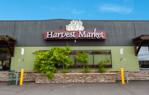Exterior of Harvest Market with green plants and a stone facade in front