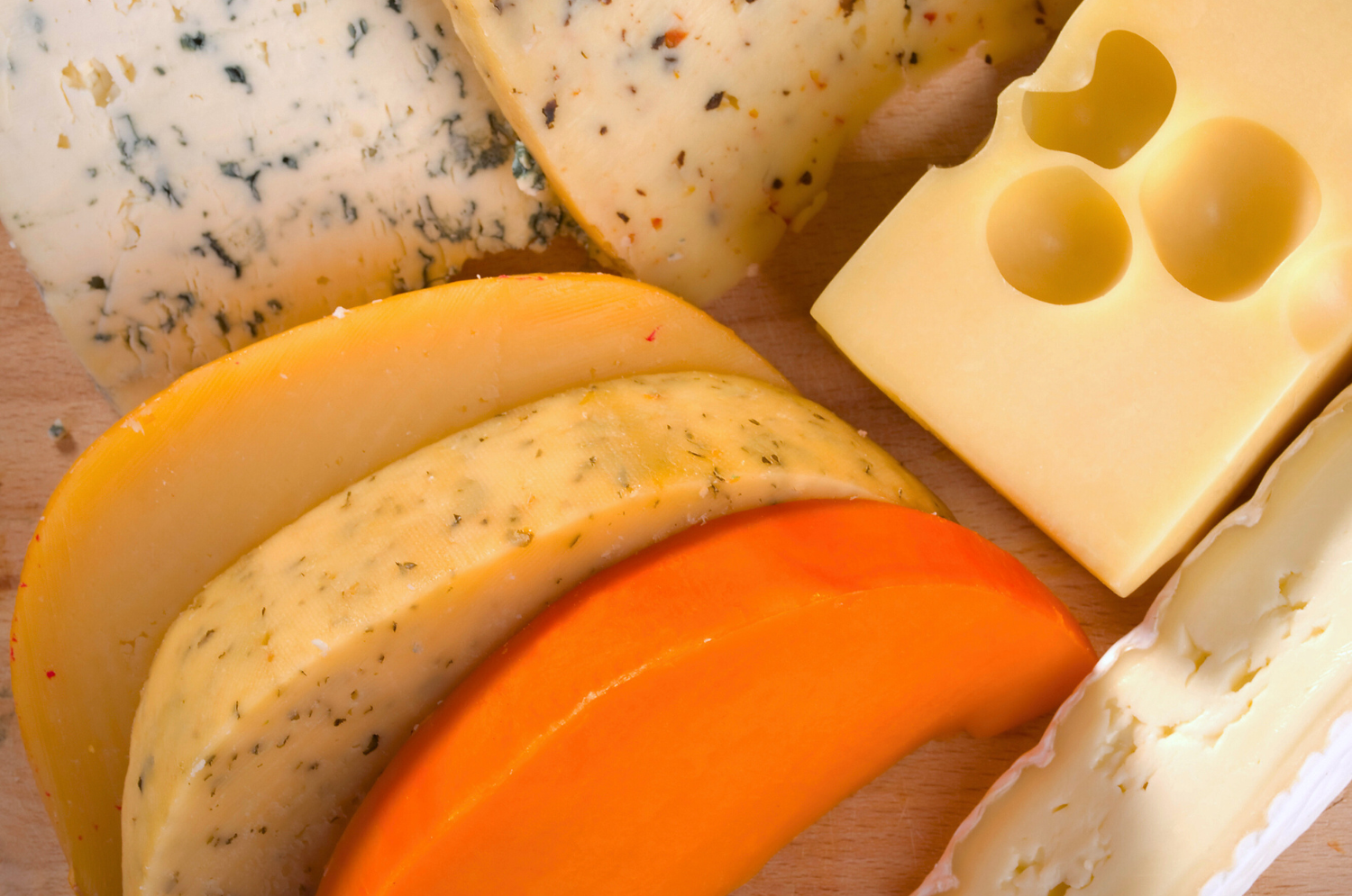 Assorted cheeses including blue cheese, pepper jack, cheddar, Swiss, and brie on a wooden surface.