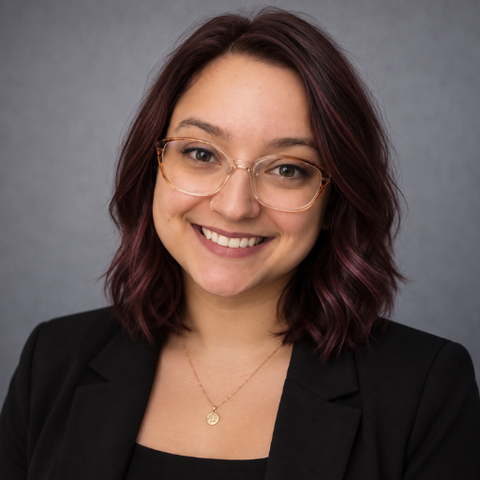Headshot of Megan. She is smiling at the camera and wearing clear glasses.