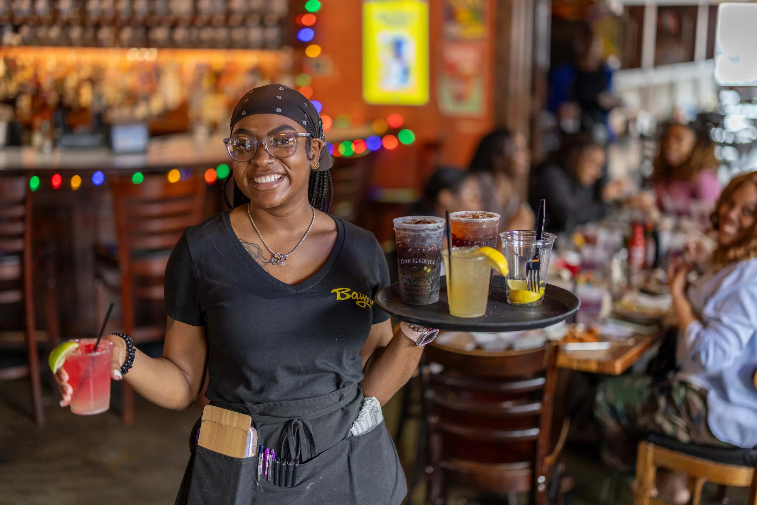 Server smiling while looking at camera and holding a tray of drinks.